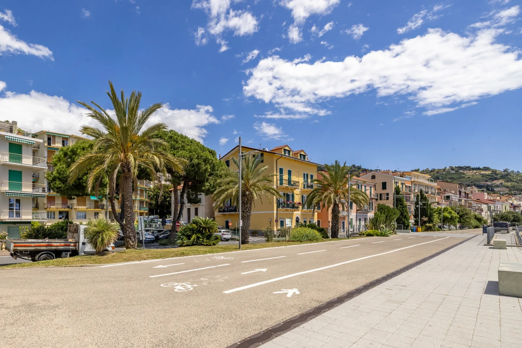 Una calle bordeada de palmeras, con edificios bajos y una amplia acera pavimentada.