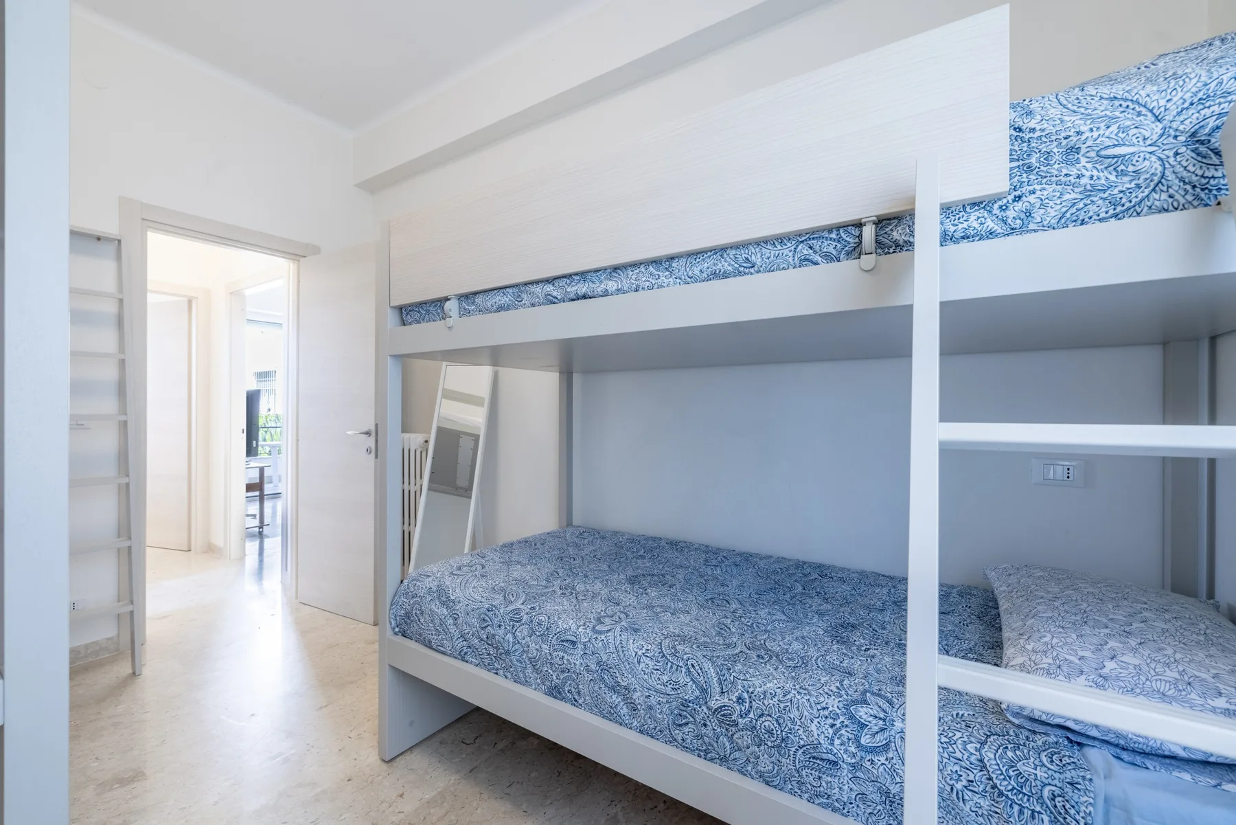 Un dormitorio luminoso con literas blancas y ropa de cama azul estampada.
