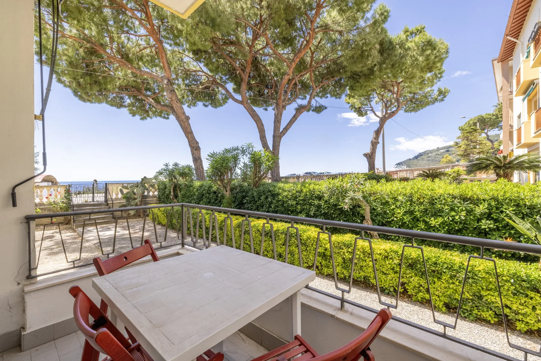 Una terraza al aire libre con mesa y asientos da a árboles y un seto verde.