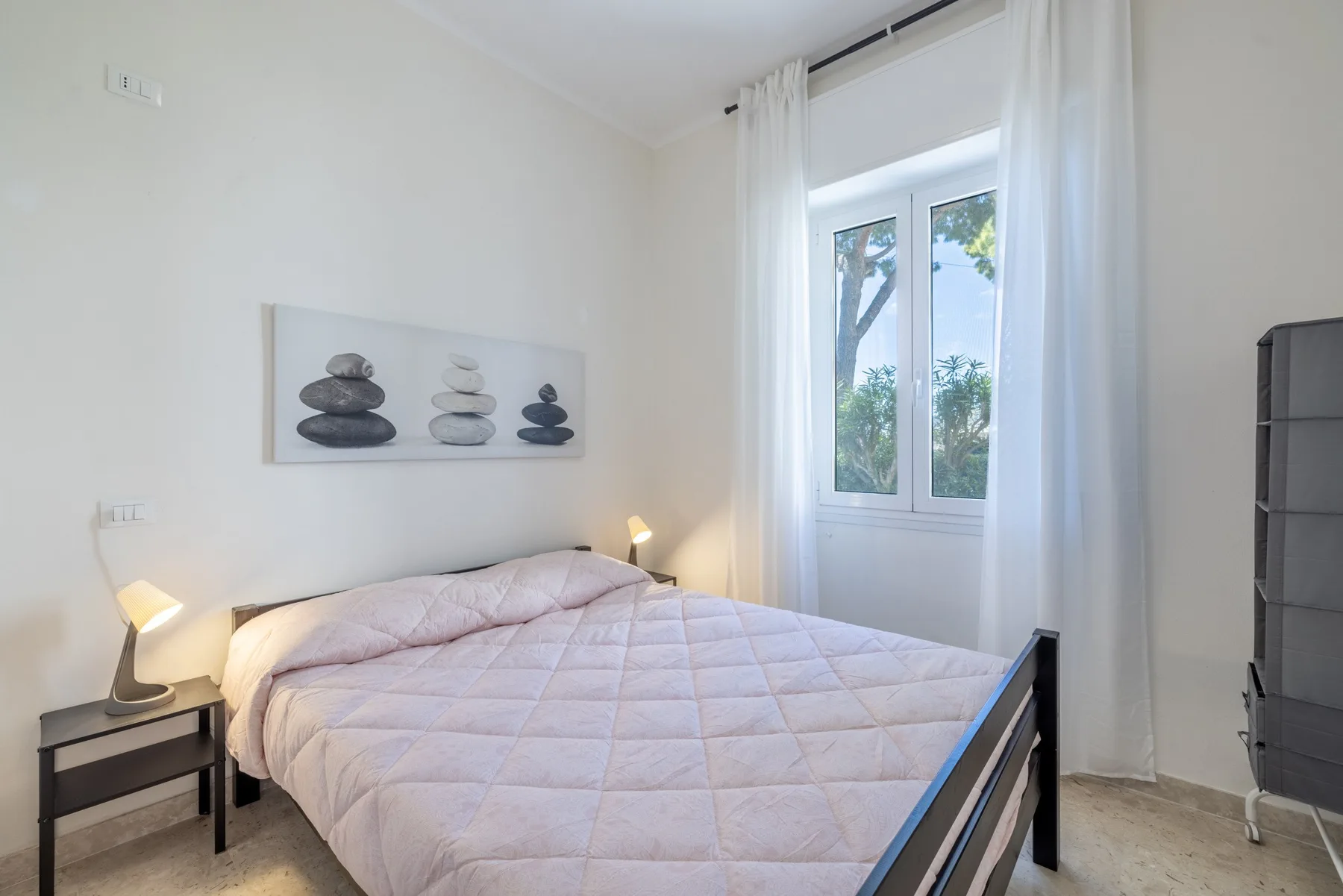 Un dormitorio con una cama, una mesita de noche y una ventana con cortinas blancas.