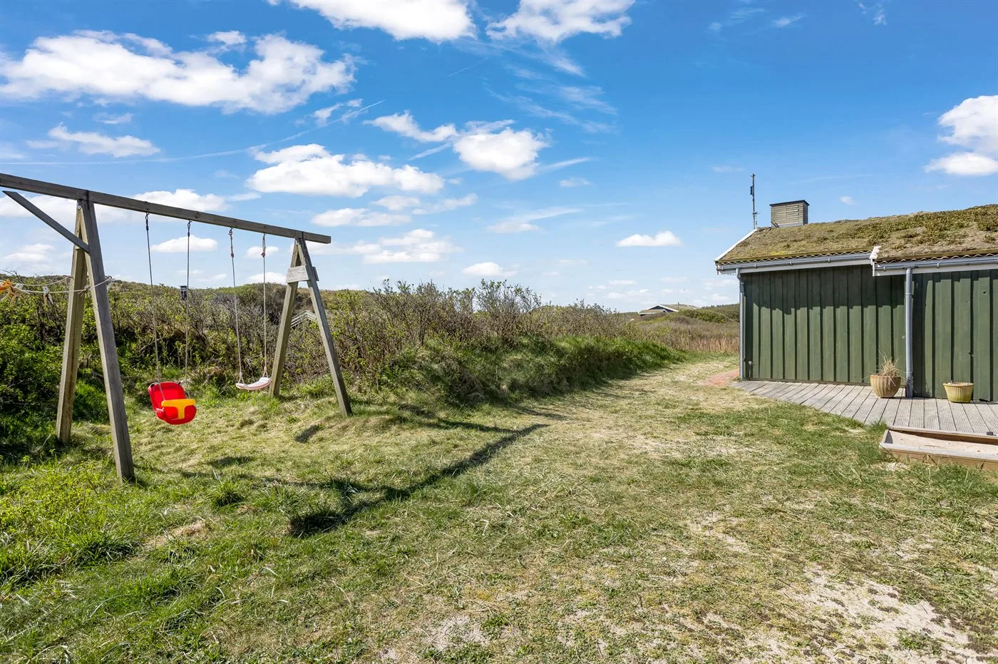 A grassy outdoor play area with a swing set beside a small shed.