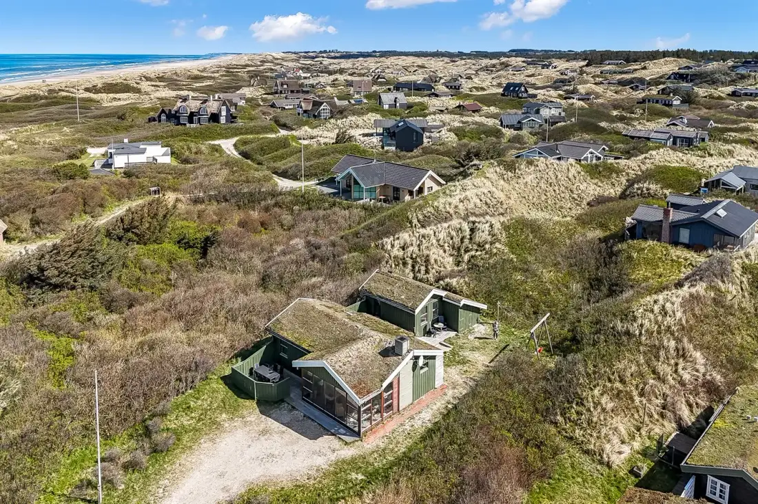 An aerial view of houses scattered across coastal dunes beside the sea.