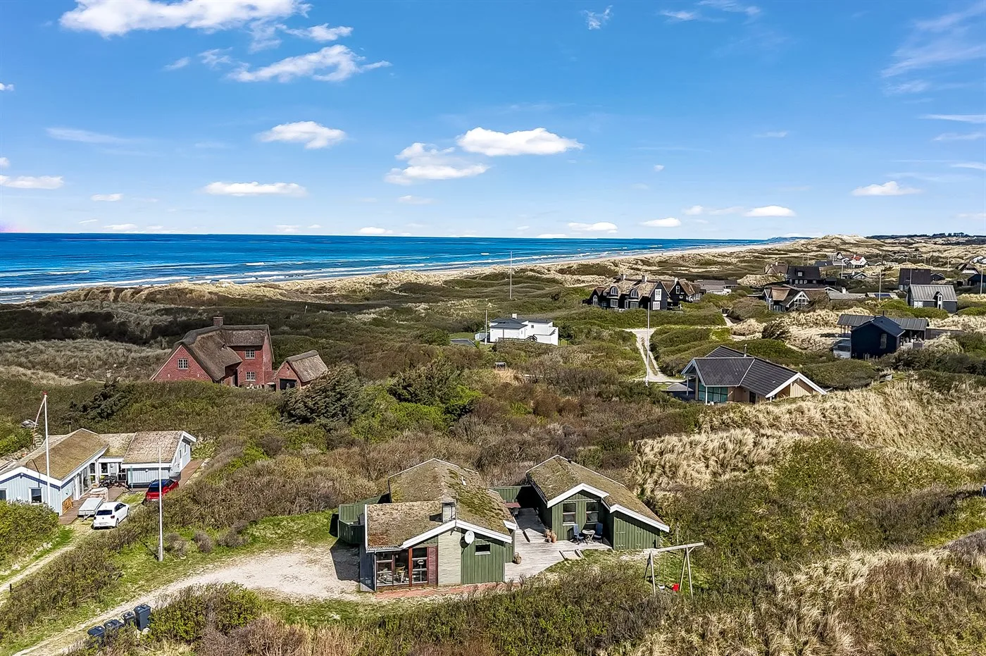 Vista aérea de un asentamiento costero con casas entre dunas y el mar al fondo.