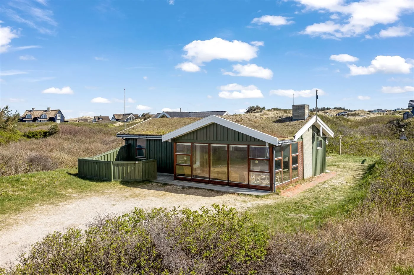 A low green building with a glass-fronted sunroom stands among grassy dunes.