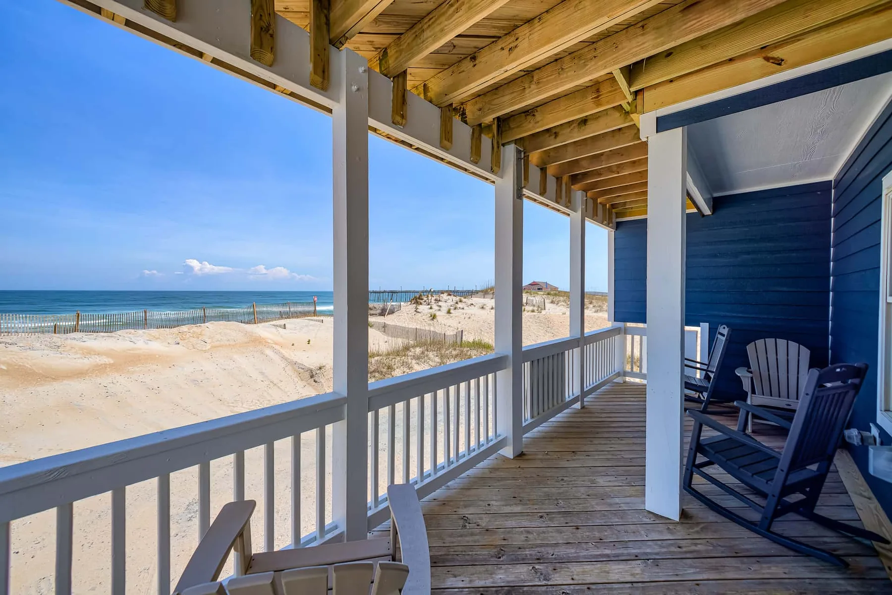 A covered wooden porch overlooks a sandy beach and the ocean.