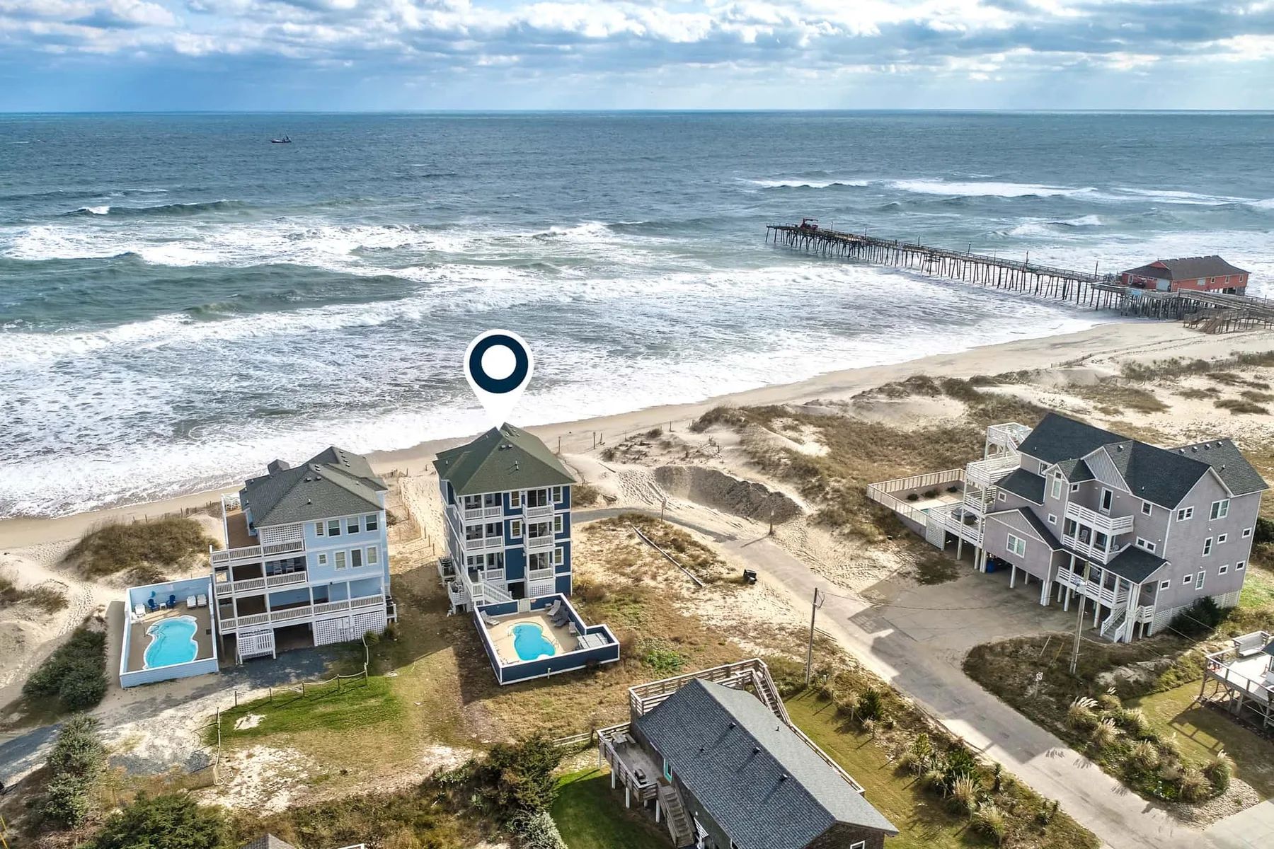 Aerial view of beachside homes beside the ocean and a wooden pier.