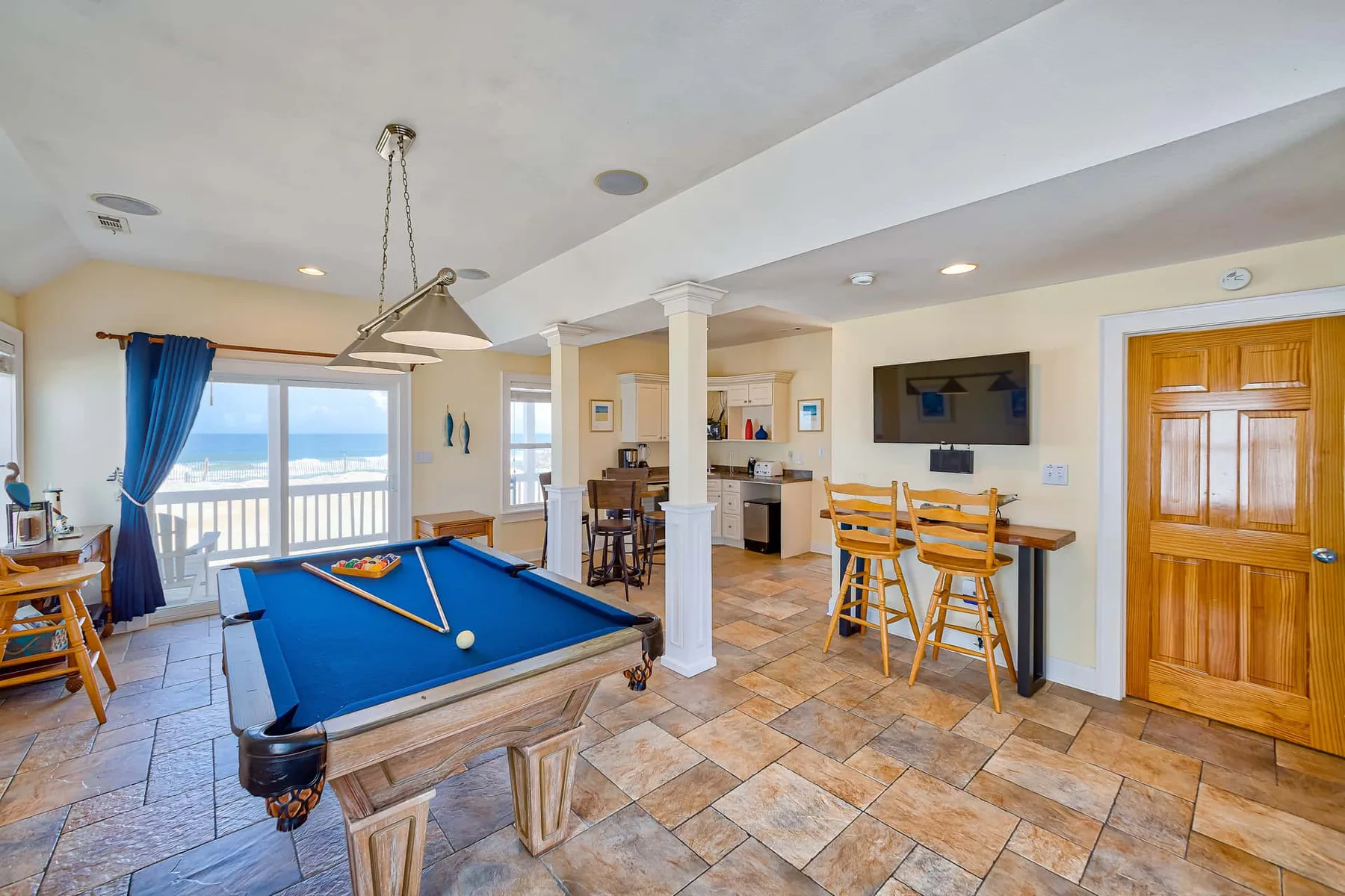 A game room with a pool table, bar seating, and large windows.