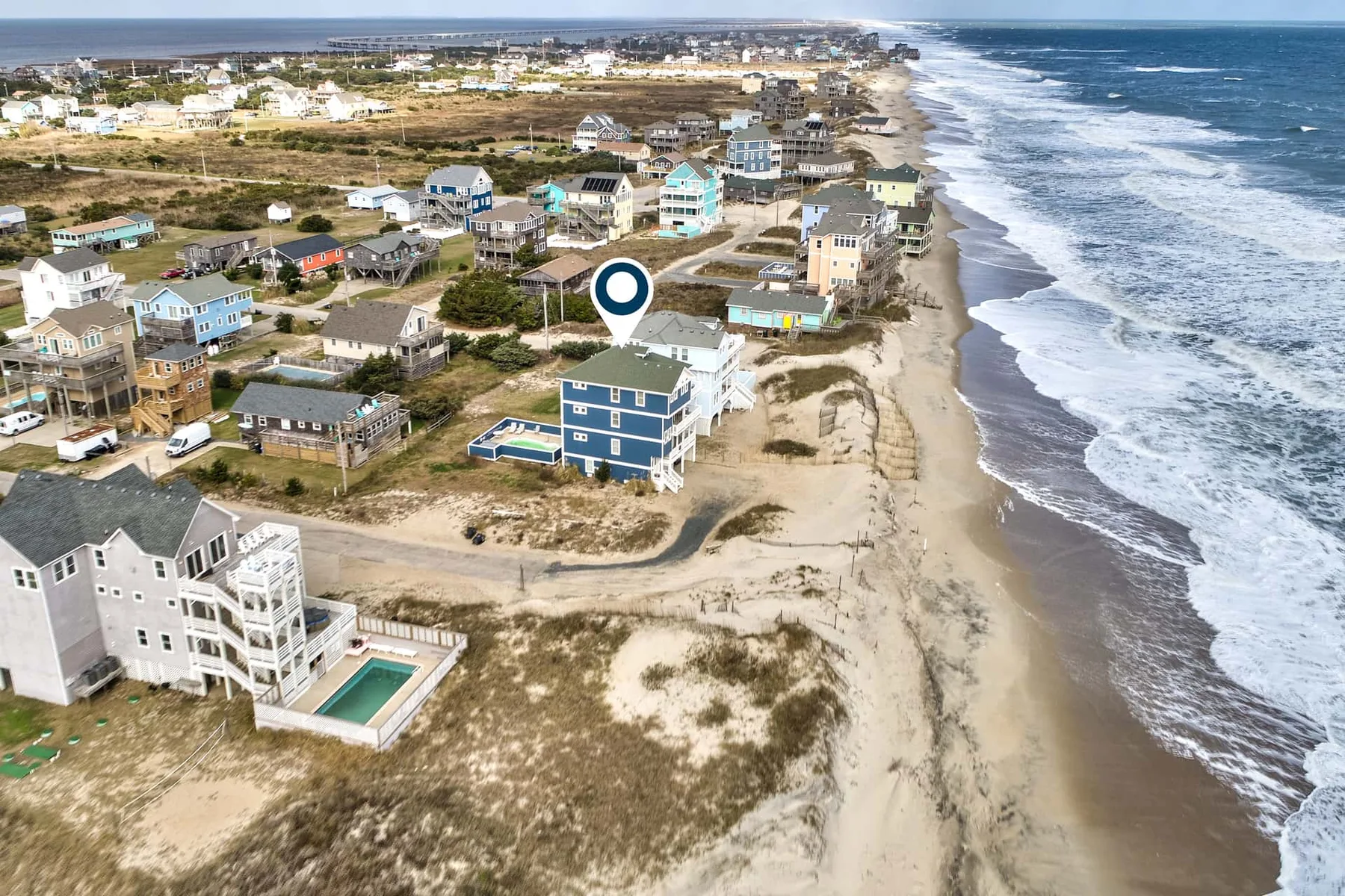 Aerial view of coastal homes beside a sandy beach and ocean.