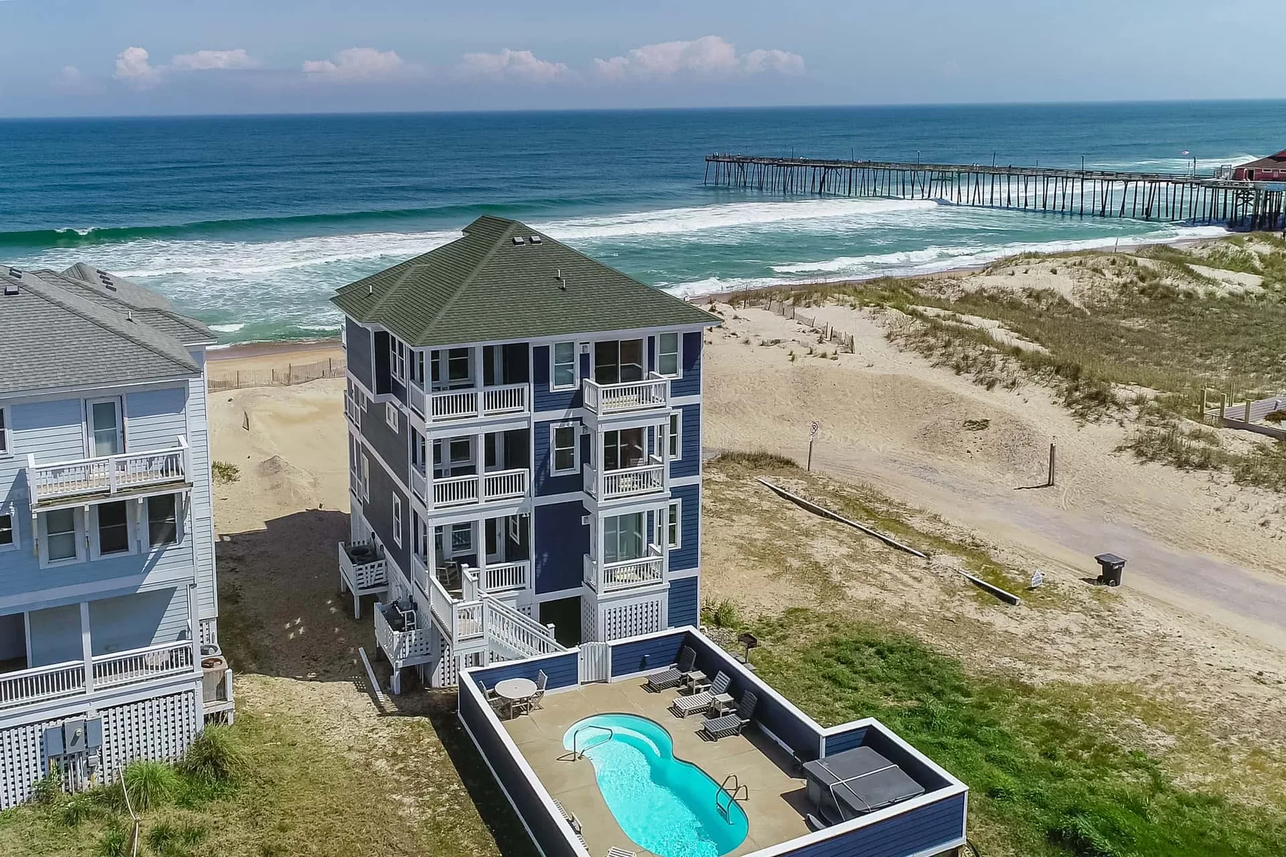 A coastal house stands beside sandy dunes, with a small pool in the foreground.