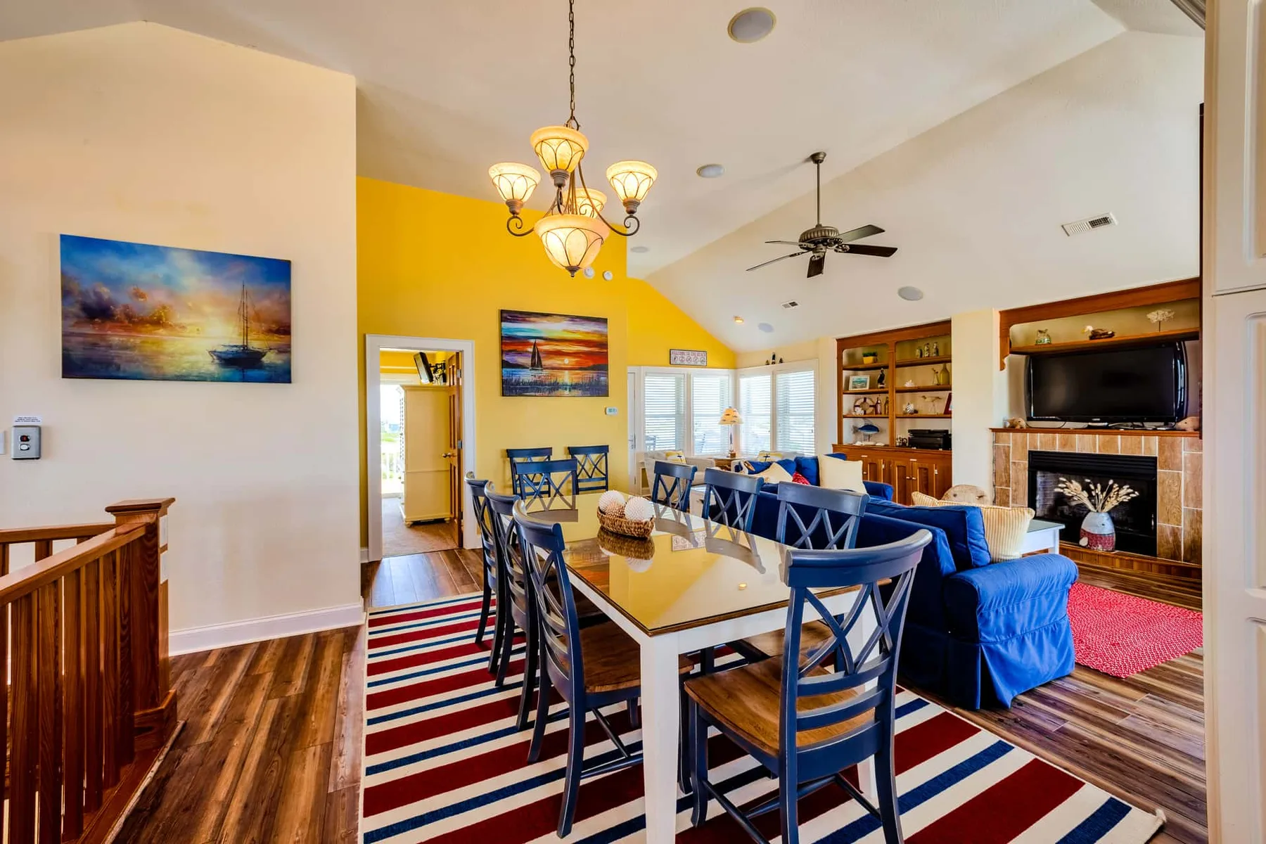 A bright dining and living area features a long table, blue seating, and a fireplace.