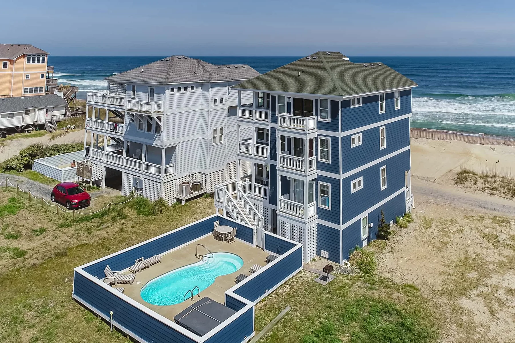 Aerial view of coastal houses beside the ocean, with a pool in the foreground.