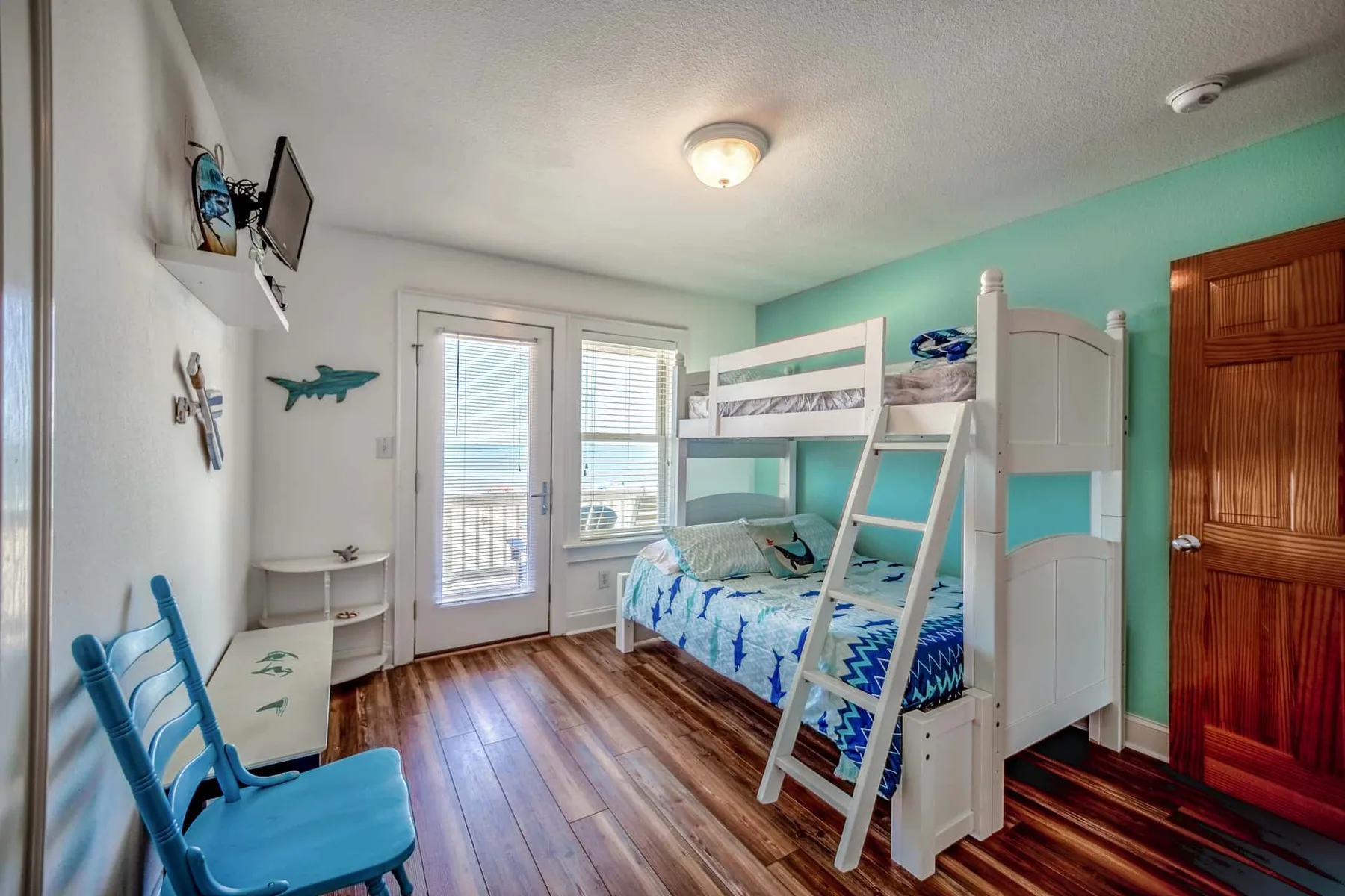 A bedroom with a bunk bed, blue seating, and windows letting in daylight.
