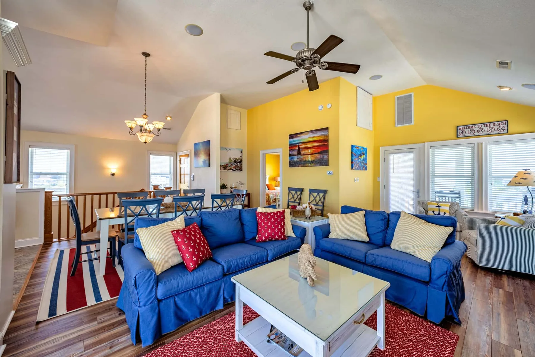 A bright living room with blue seating, a coffee table, and an open dining area.