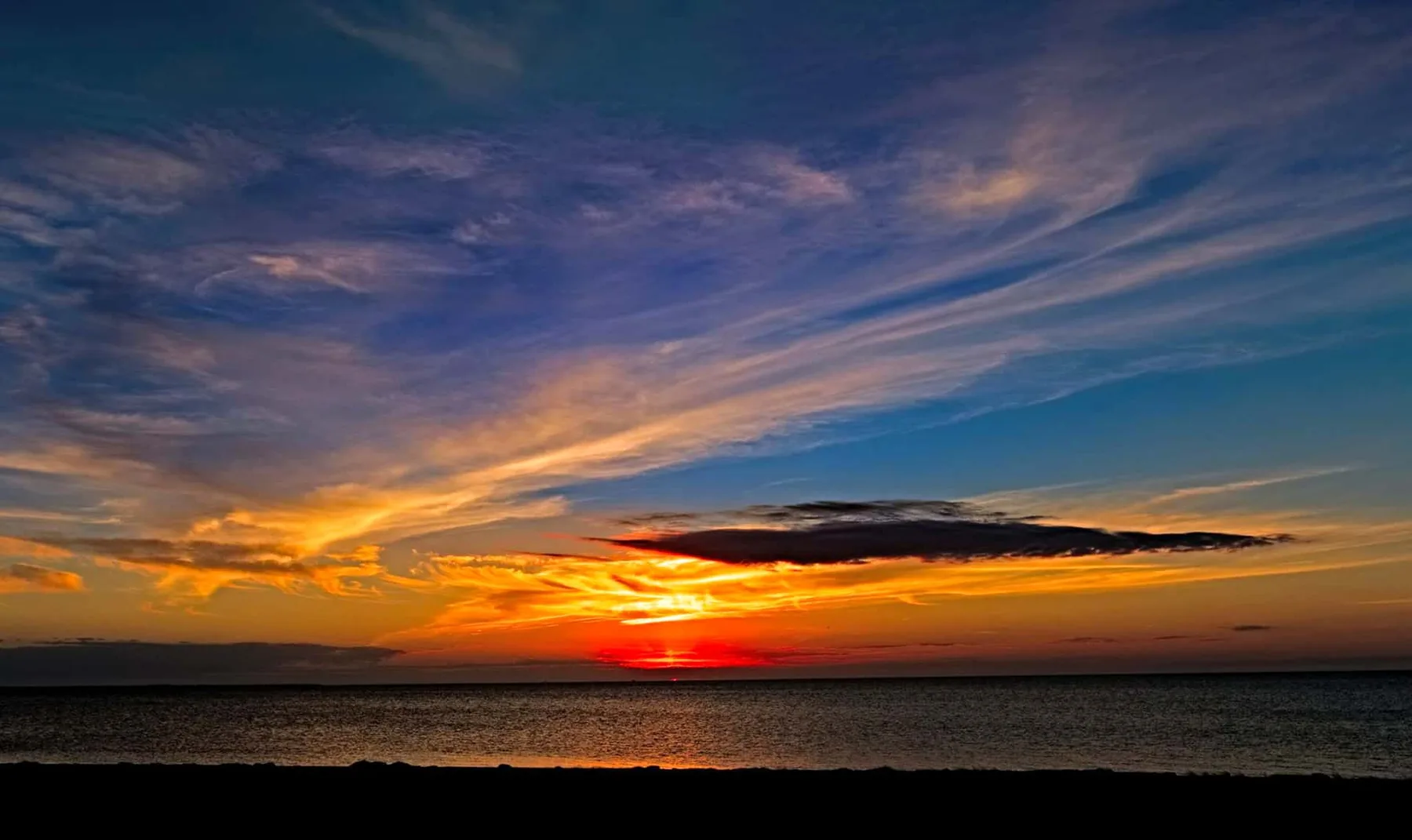 A sunset glows over the ocean beneath streaked clouds.