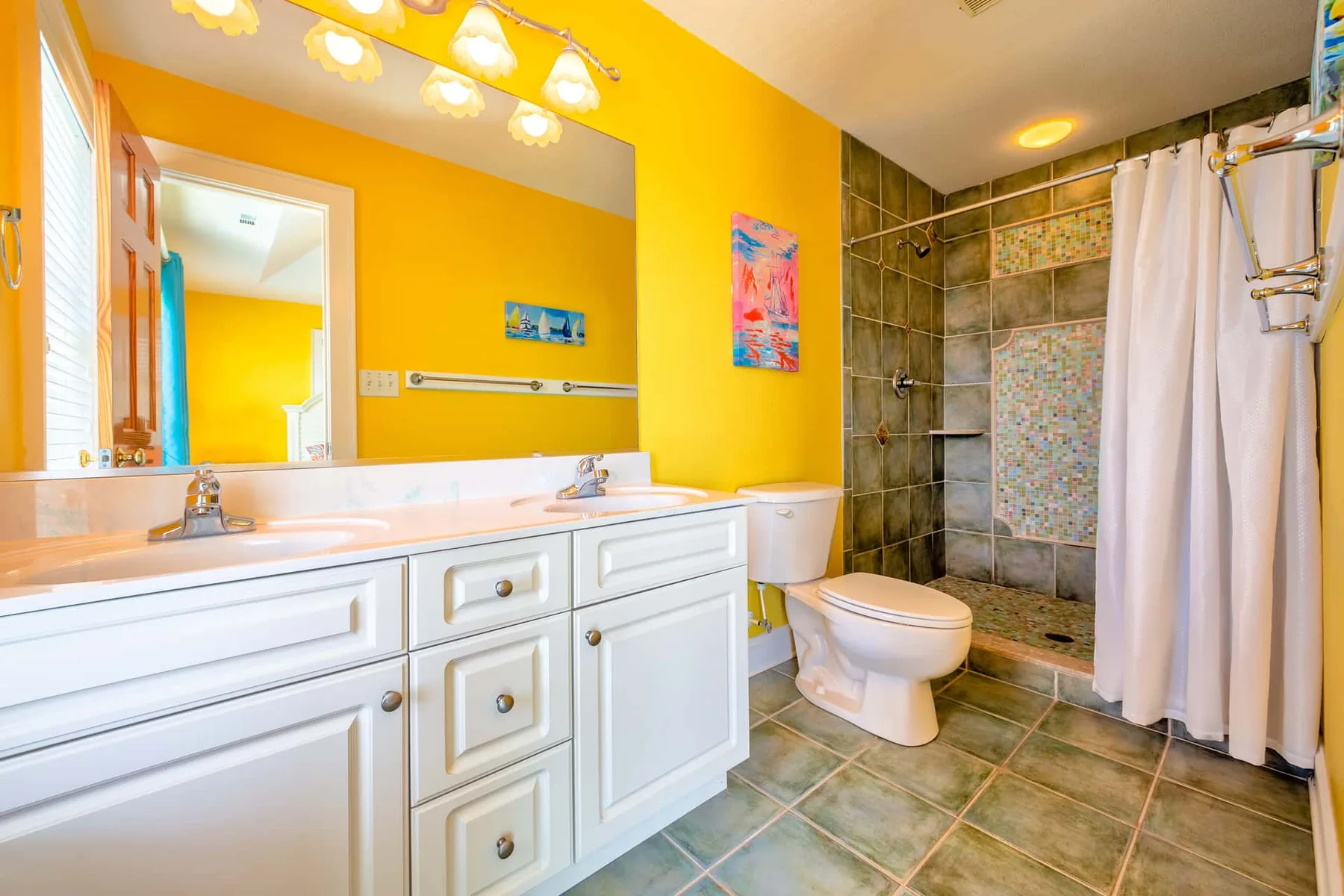 A bright bathroom with a long white vanity and a tiled shower area.