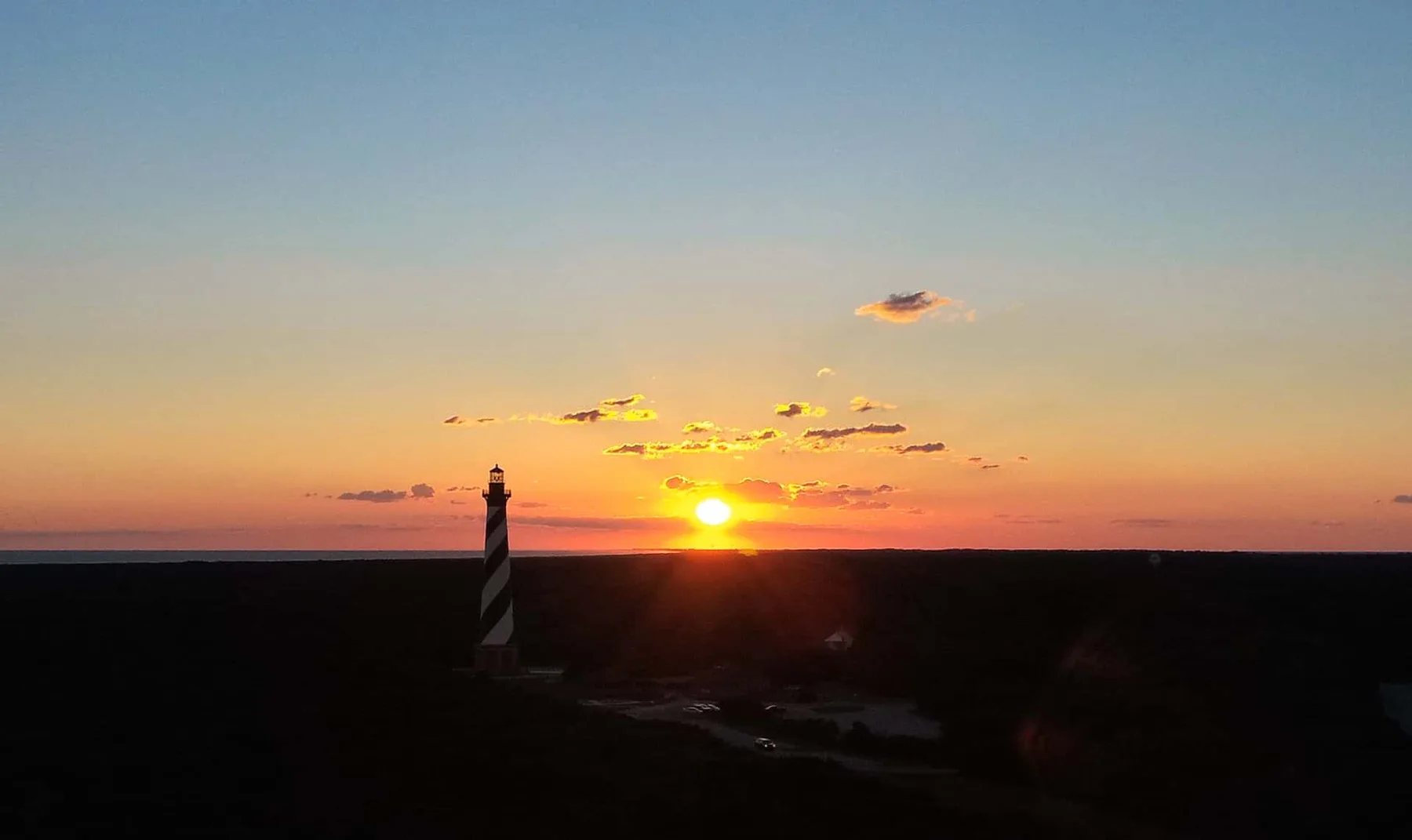 A lighthouse stands against a colorful sunset over a flat horizon.