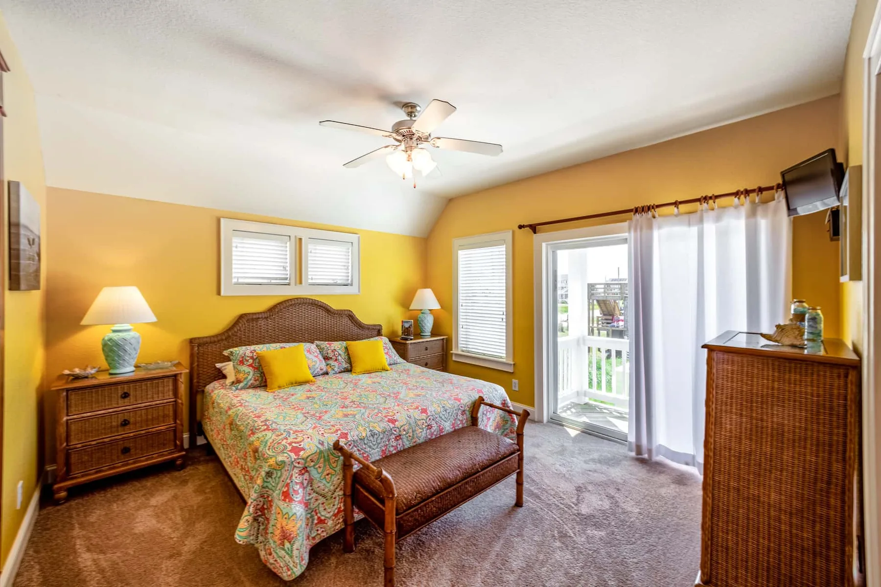 A bright bedroom with a floral bedspread and glass doors opening to a balcony.