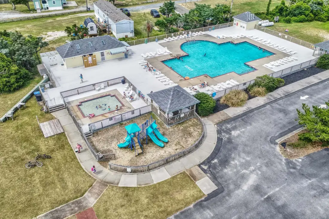 An outdoor pool area with a turquoise pool and a small playground.