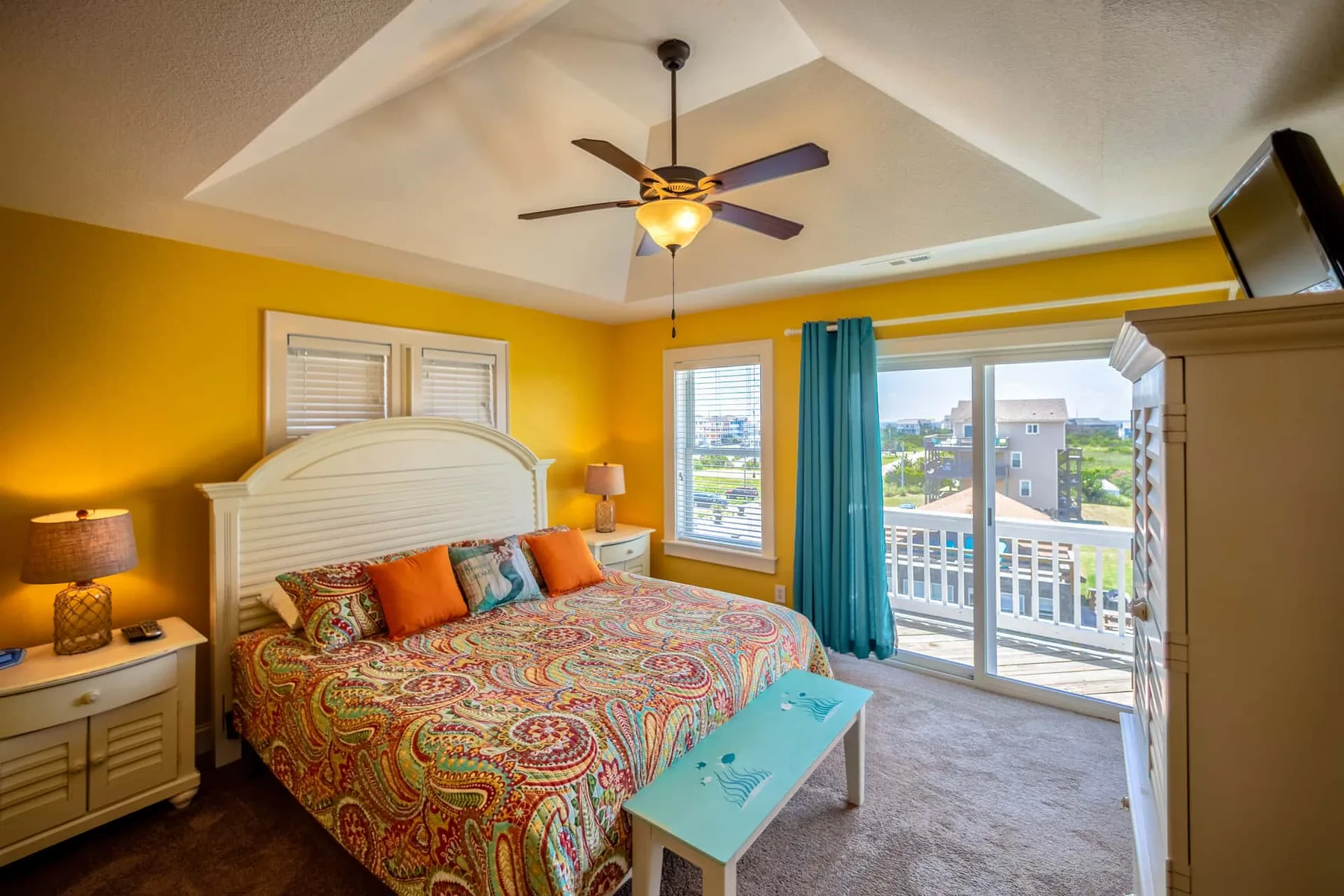 A colorful bedroom with a patterned bedspread and glass doors opening onto a balcony.