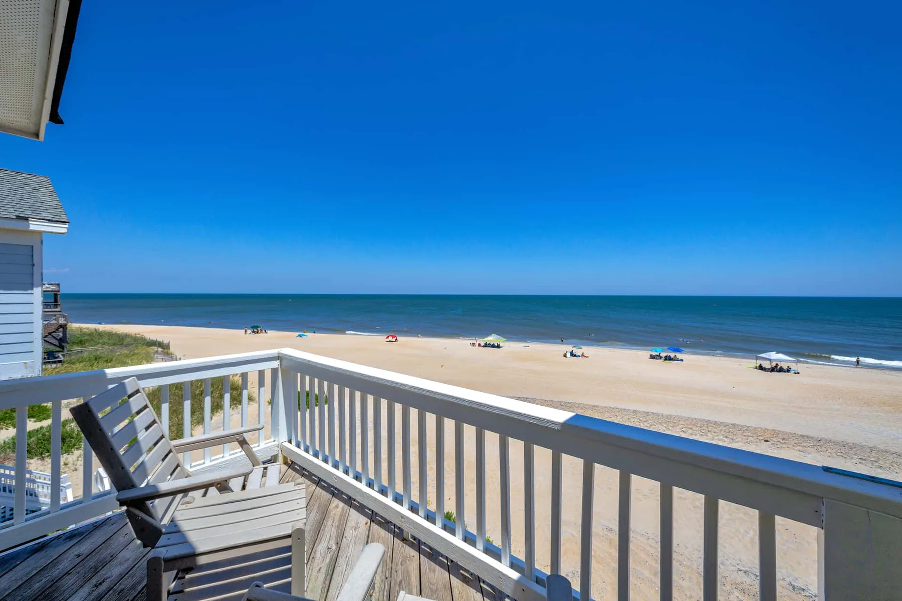 A wooden balcony overlooks a sandy beach and the ocean.