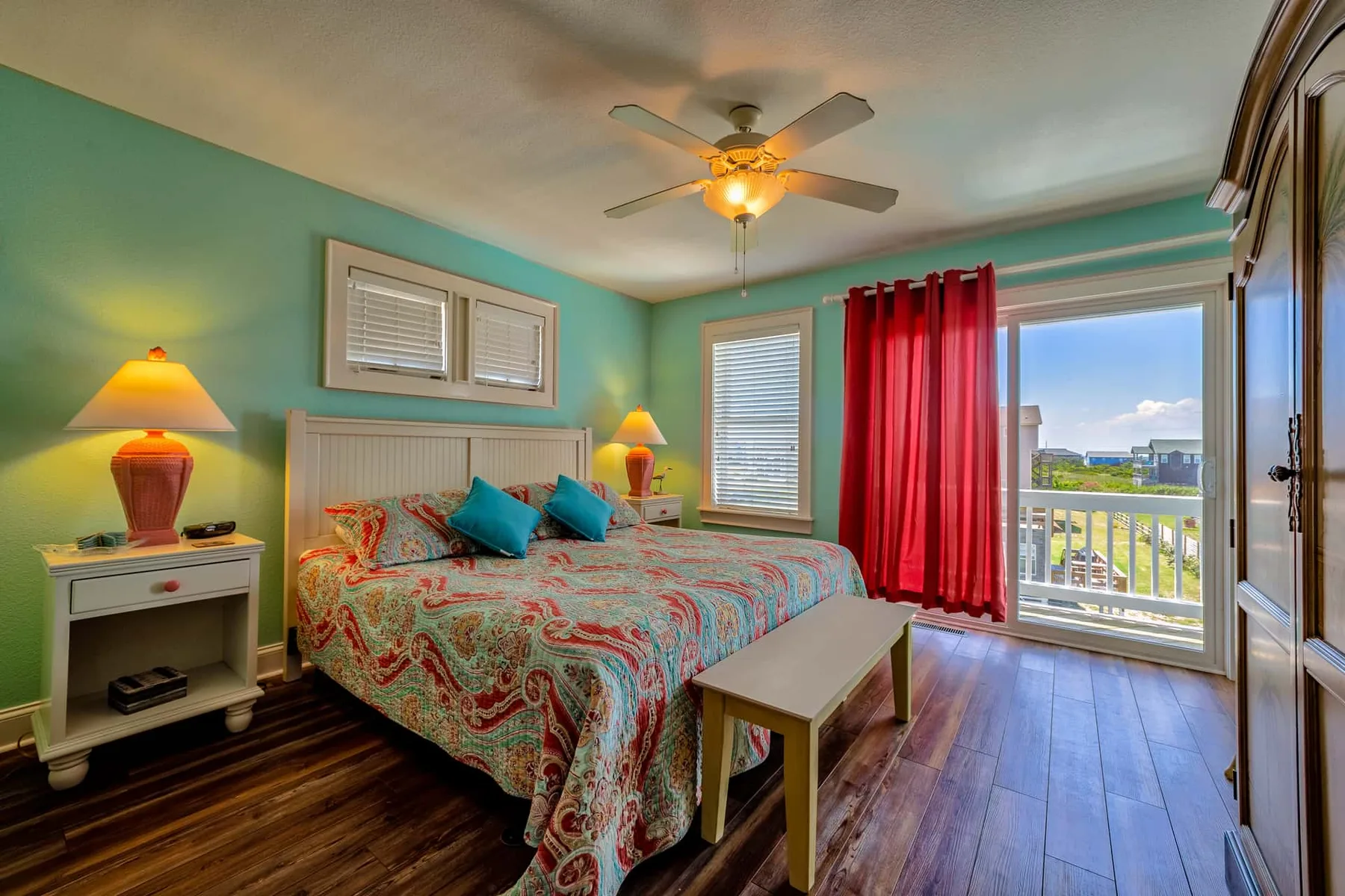 A bedroom with a bed, ceiling fan, and red curtains beside a glass balcony door.