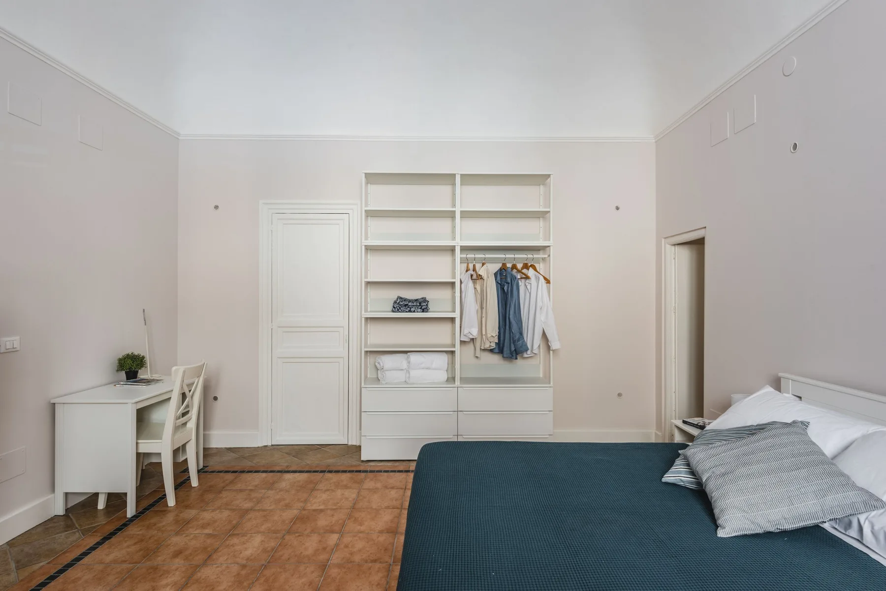Un dormitorio con una cama junto a estantes abiertos y ropa colgada.