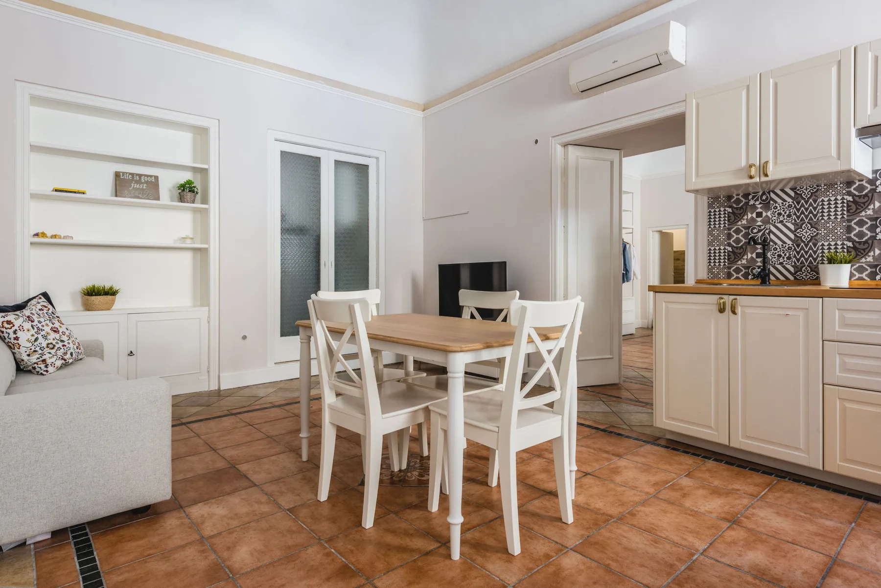 Un comedor luminoso con una mesa de madera y asientos blancos junto a la cocina.