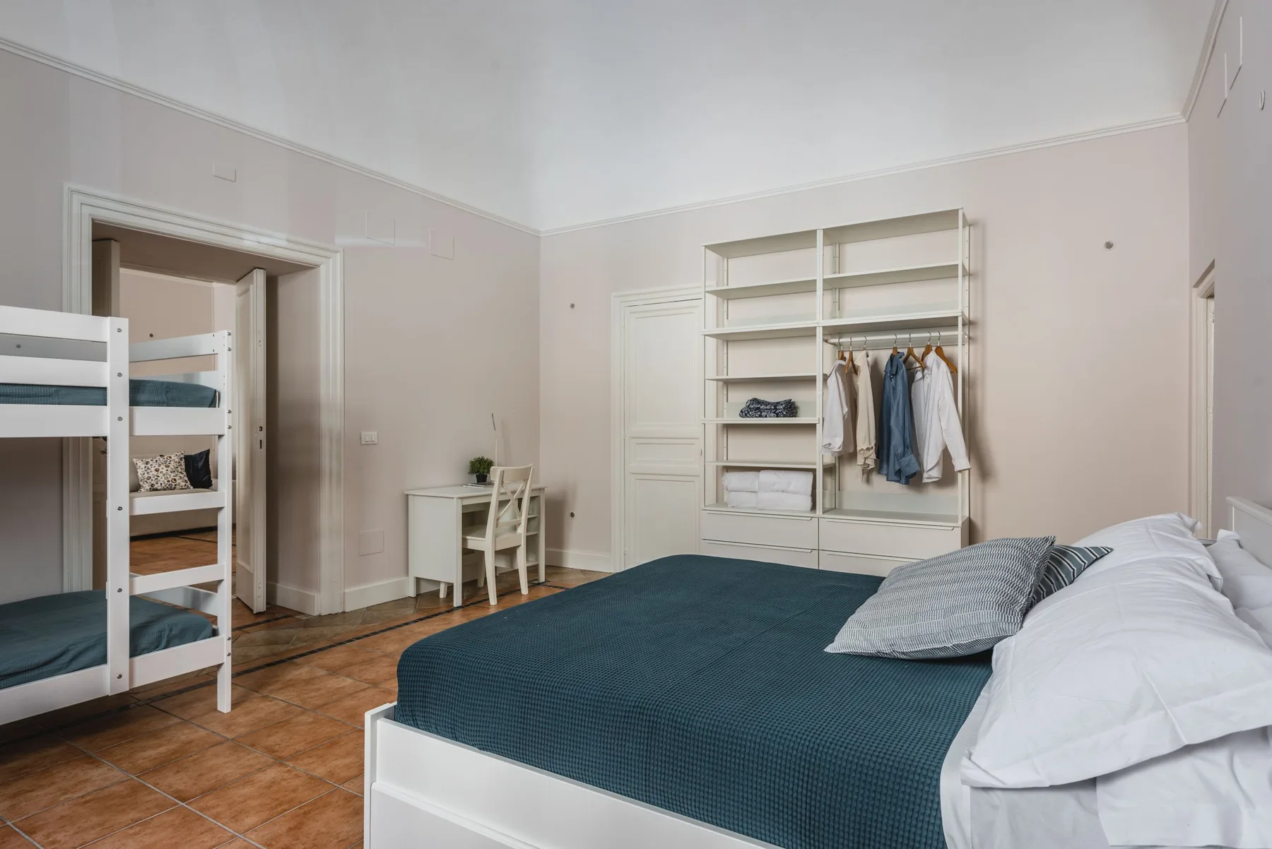 Un dormitorio con una cama grande, una litera y estanterías abiertas.
