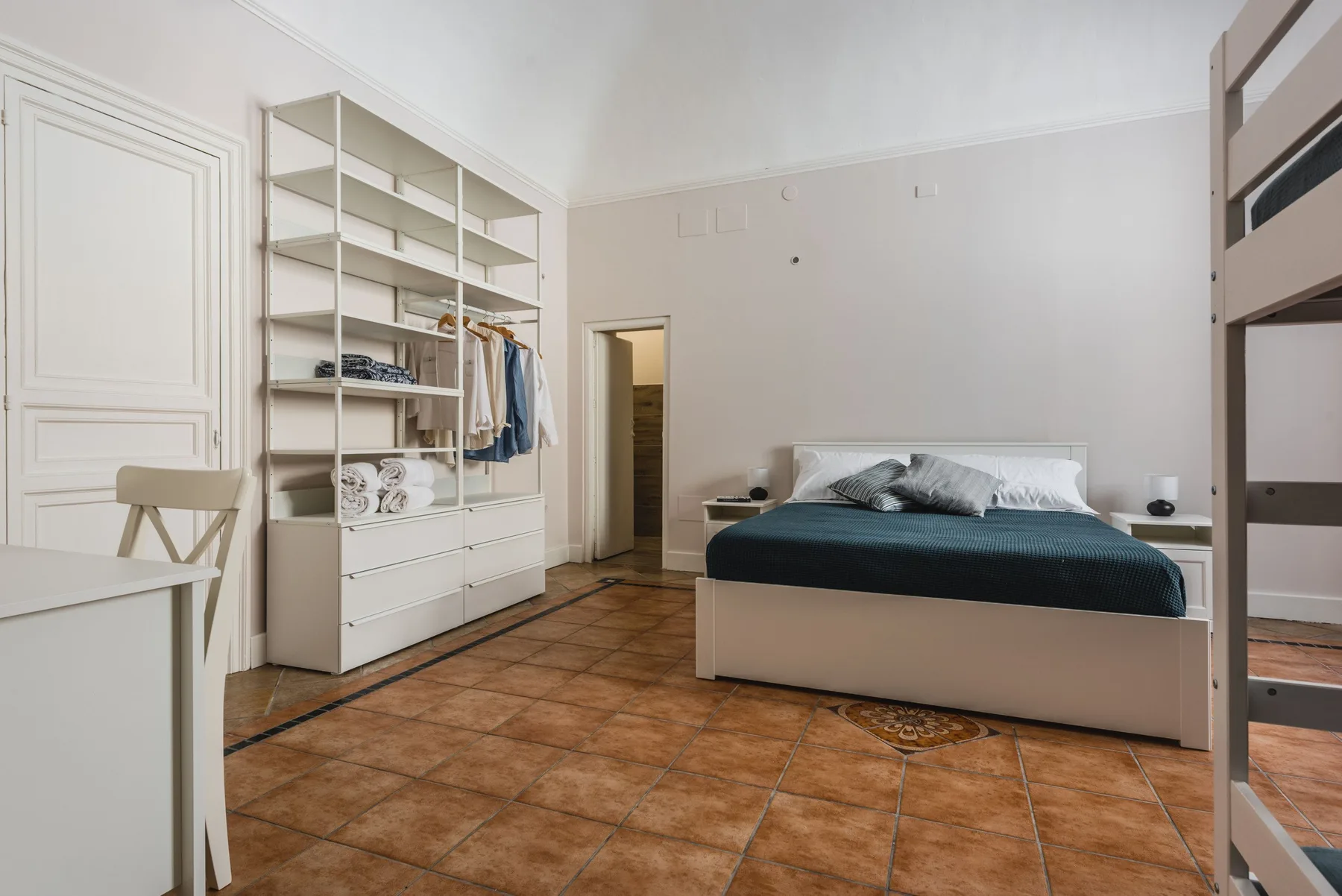 Un dormitorio con una cama, estanterías abiertas y baldosas de color terracota.