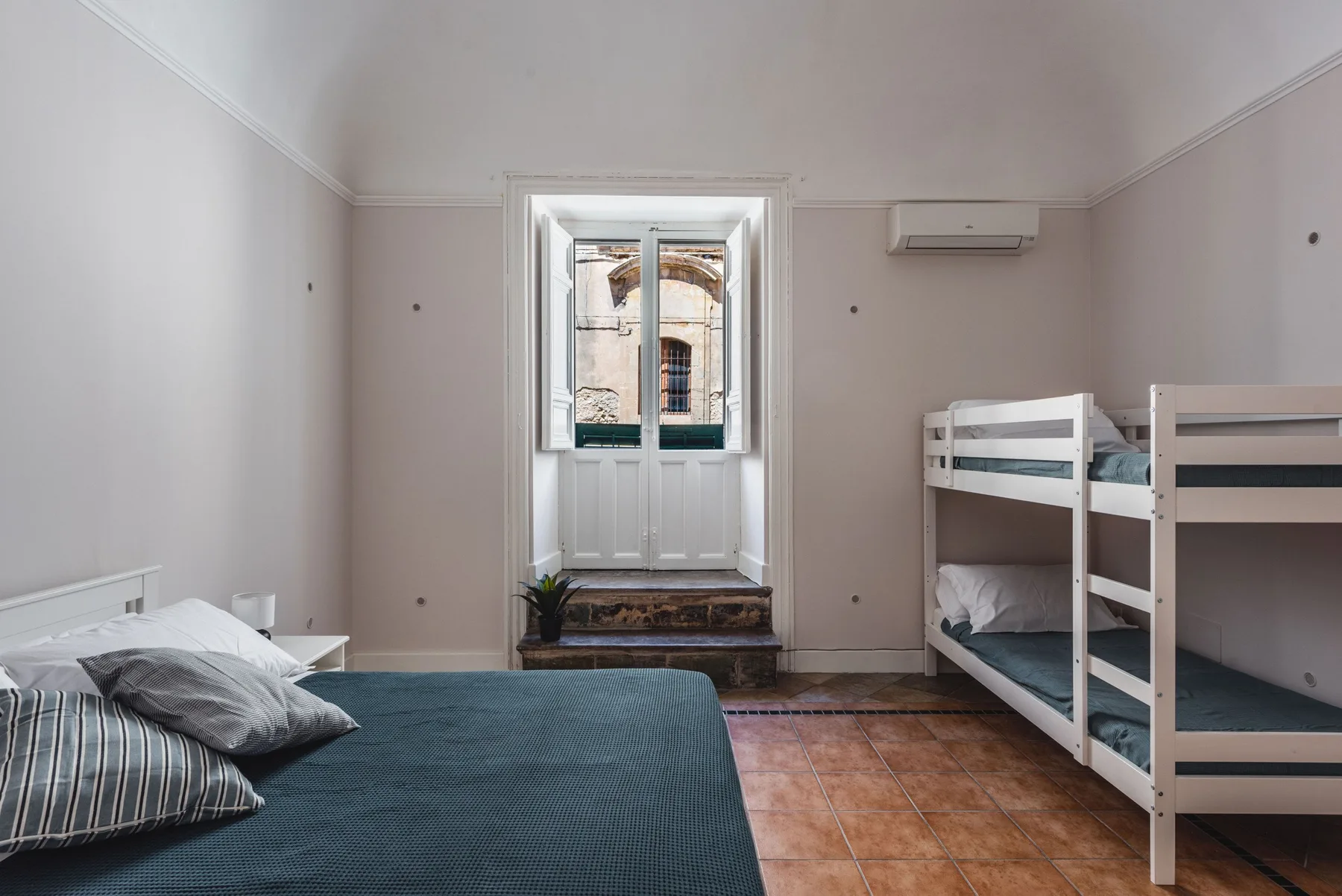 Un dormitorio con literas y una cama baja junto a una ventana alta.