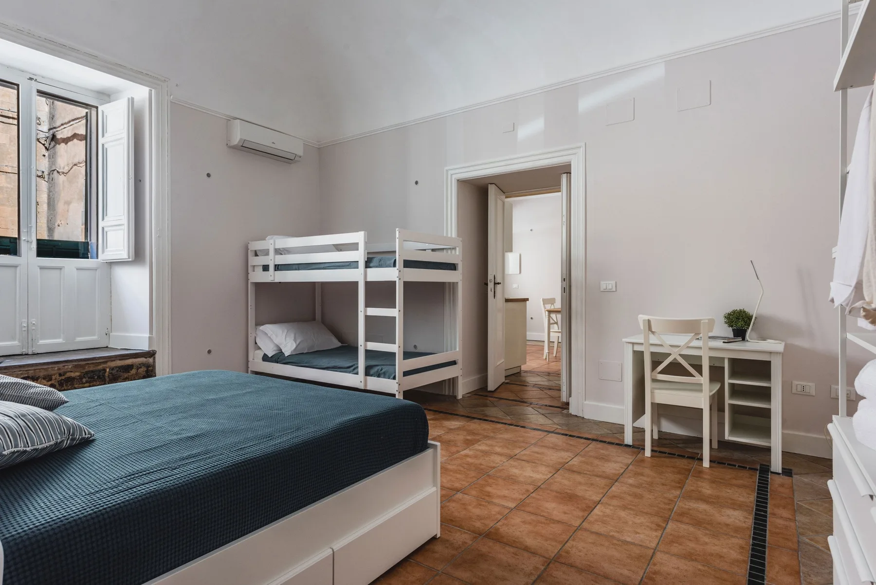 Un dormitorio con una cama, literas y un pequeño escritorio.