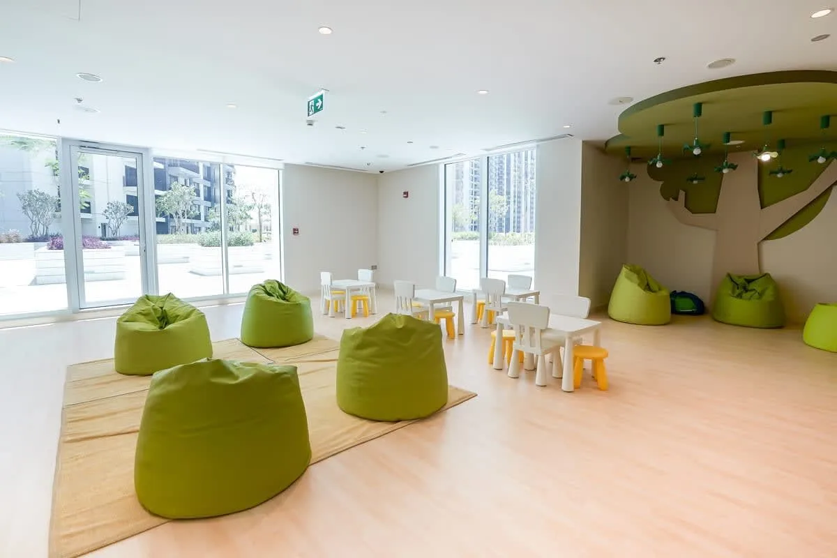 Una sala luminosa con asientos verdes y mesas pequeñas junto a grandes ventanas.