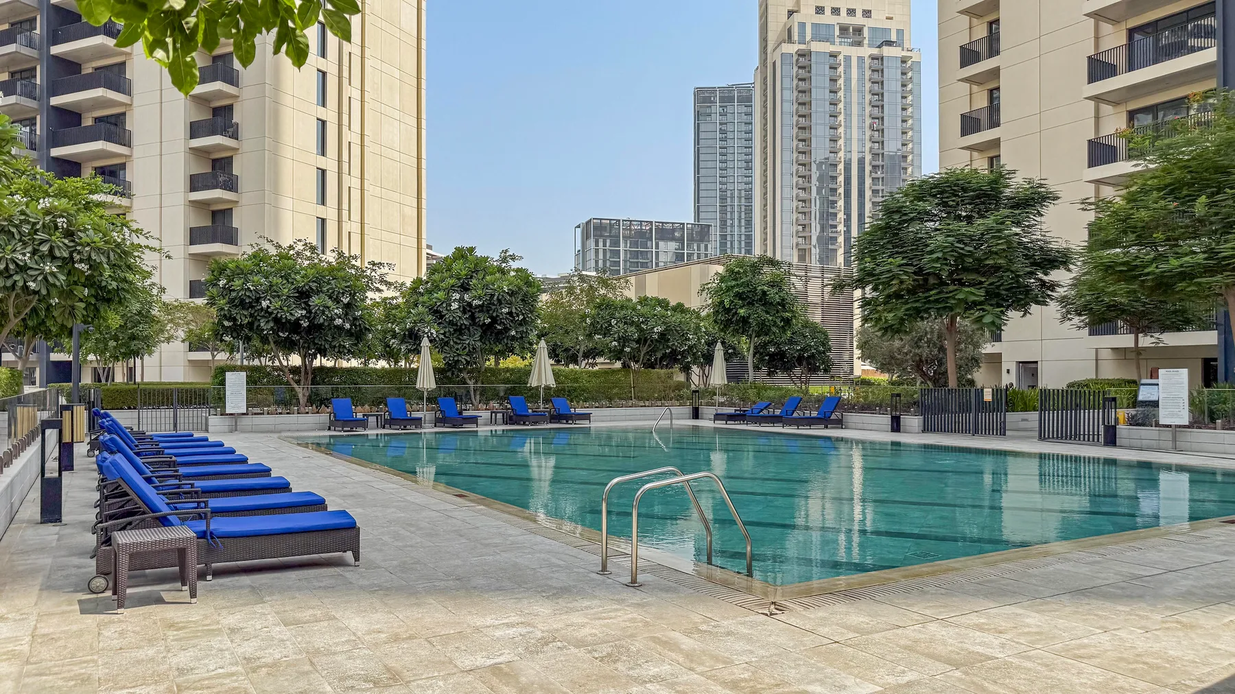 Una piscina al aire libre está rodeada de tumbonas y edificios residenciales altos.