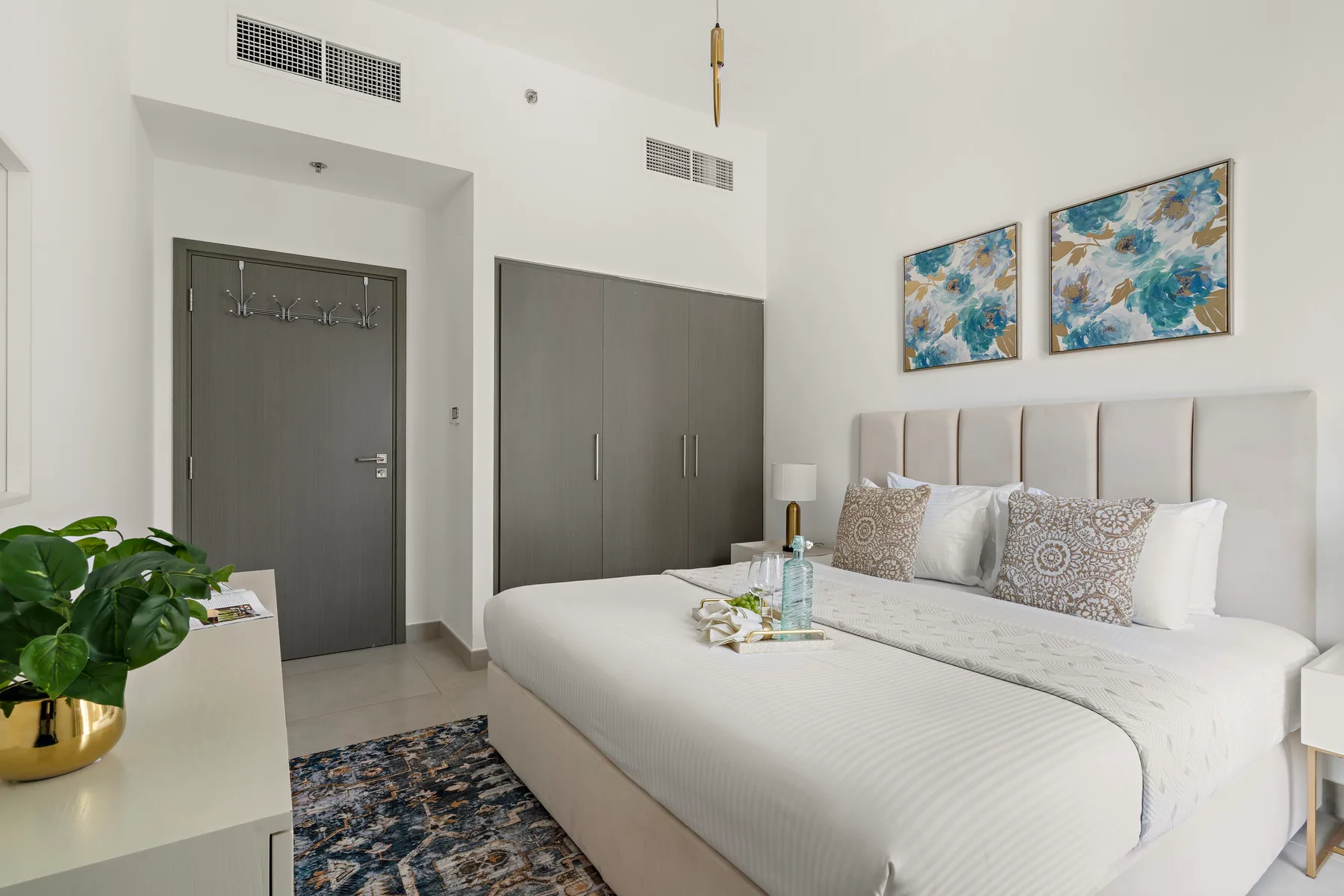 Un dormitorio luminoso con una cama grande, cojines estampados y cuadros coloridos sobre el cabecero.