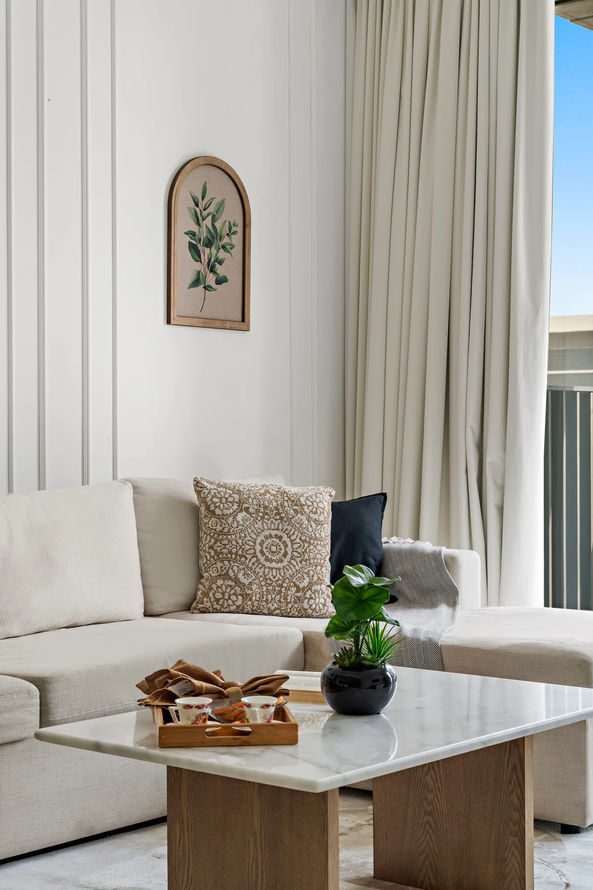 Una sala luminosa con asientos claros, una mesa de centro y cortinas largas.