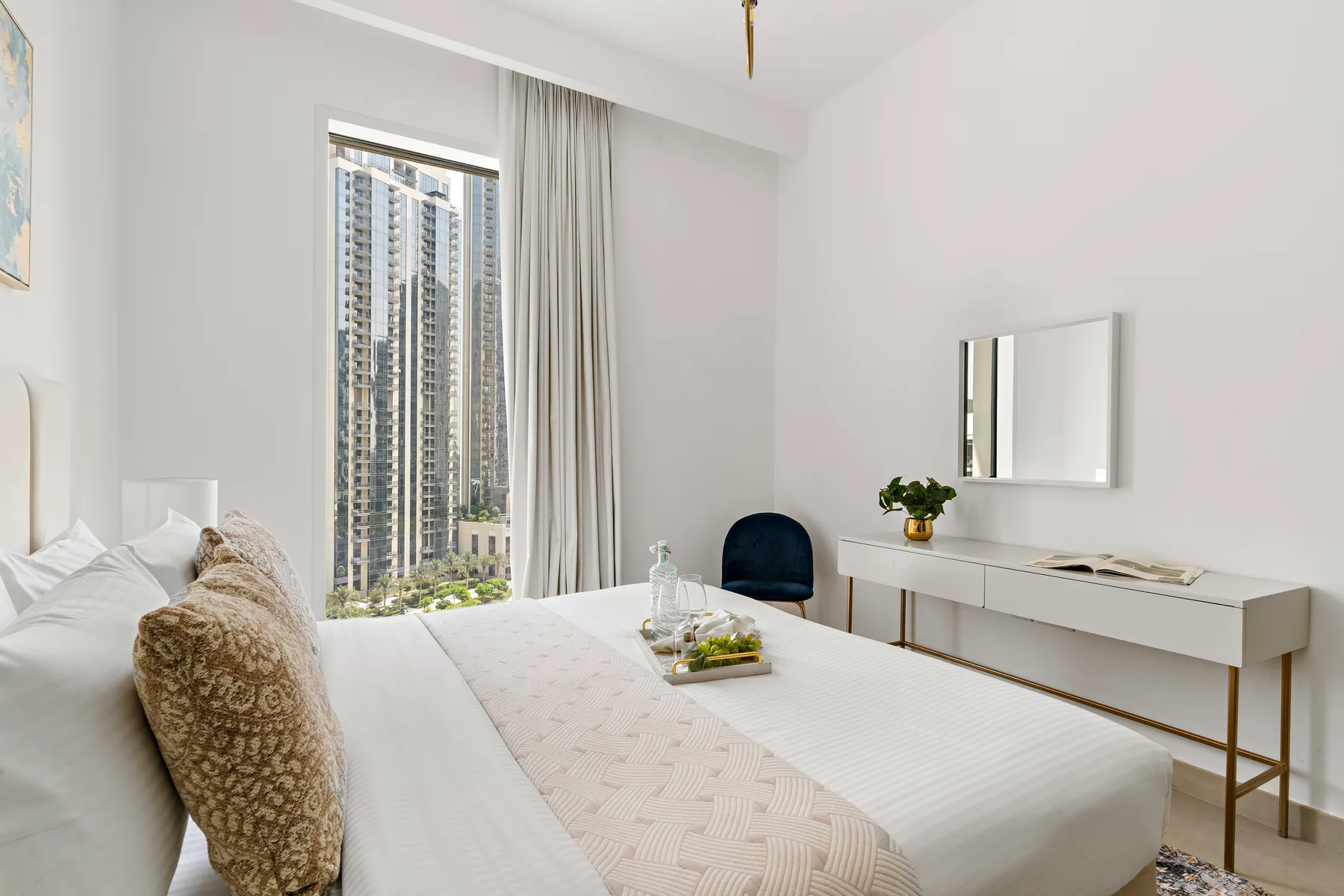 Un dormitorio luminoso con una cama grande junto a una ventana con vistas a edificios altos.
