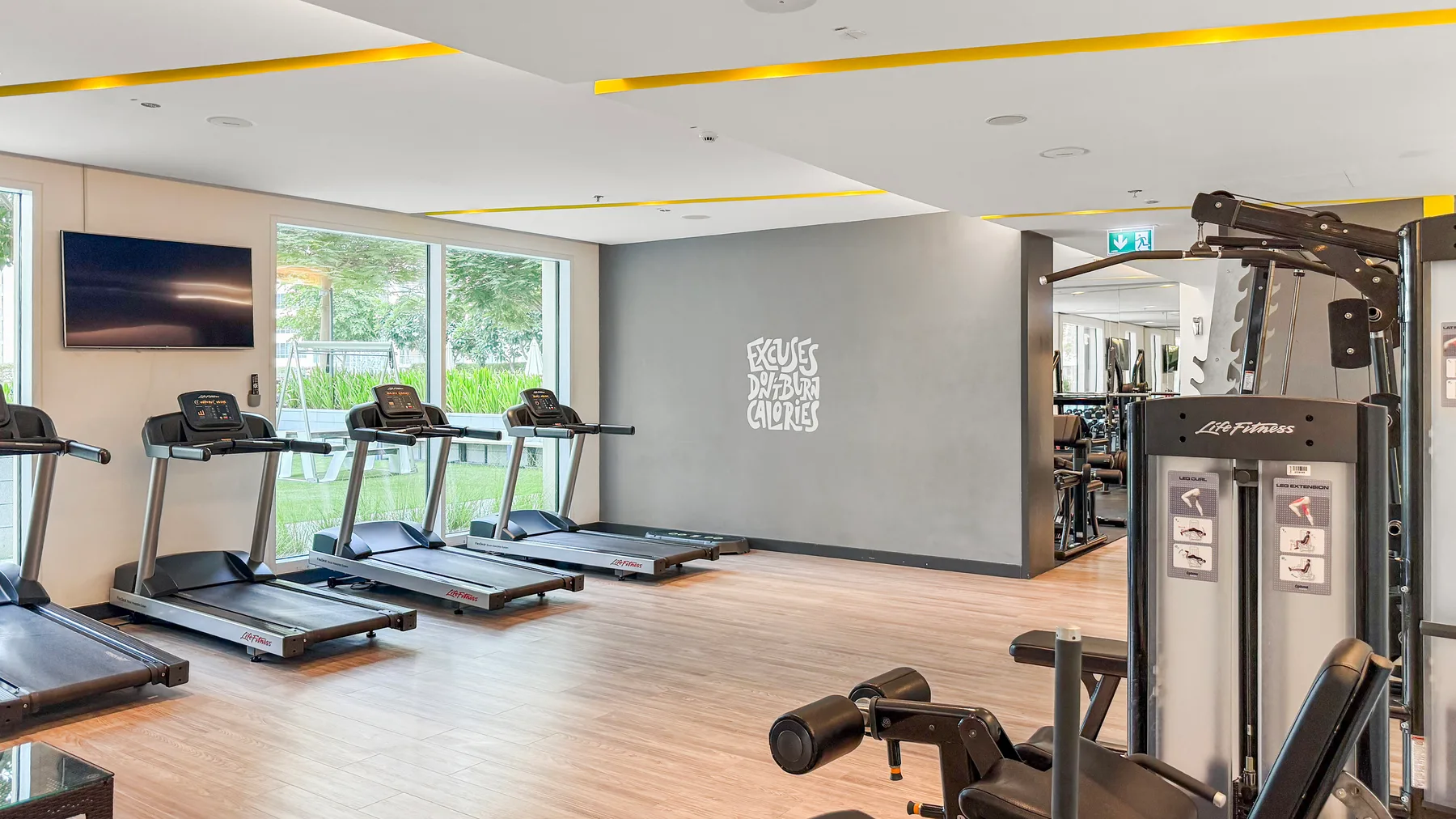 Un gimnasio con cintas de correr junto a las ventanas y máquinas de ejercicio.