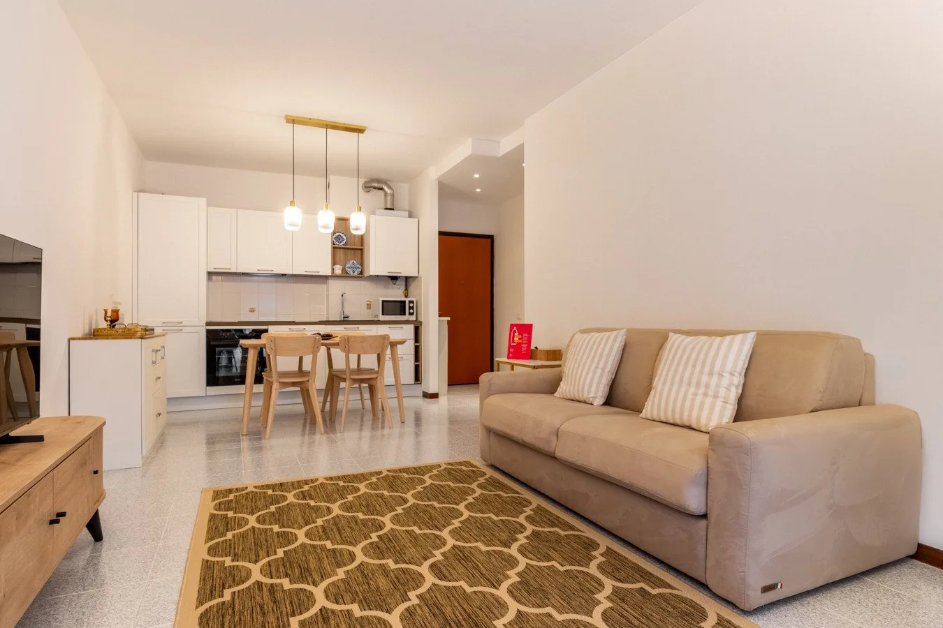 Una sala de estar y cocina de concepto abierto con un sofá beige y una mesa de comedor.