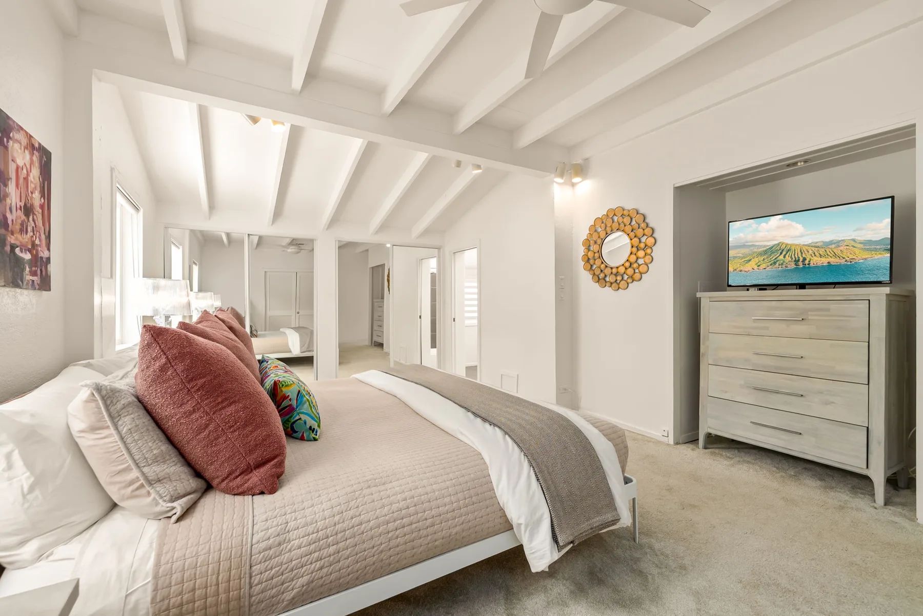 Un dormitorio luminoso con una cama tendida y una cómoda debajo de un televisor.