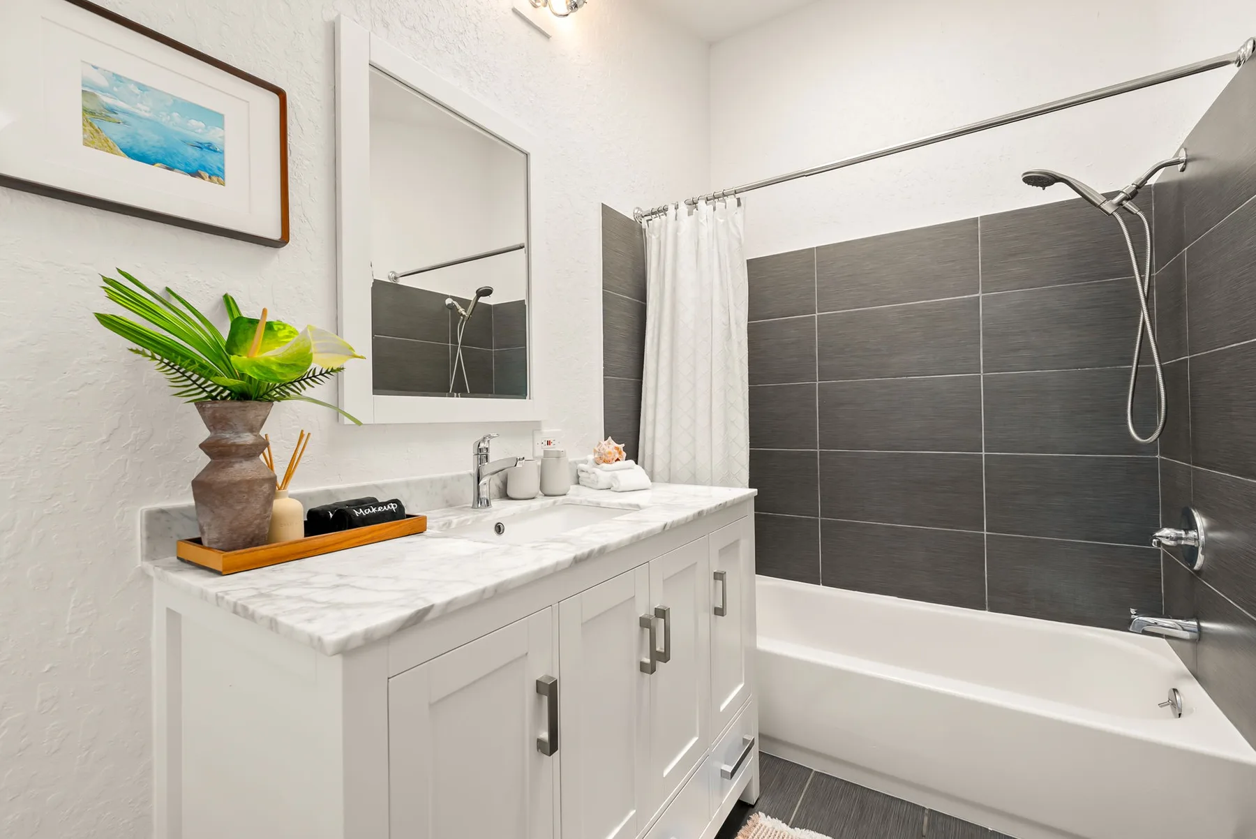 Un baño con un tocador blanco, paredes de azulejos oscuros y una bañera con ducha.