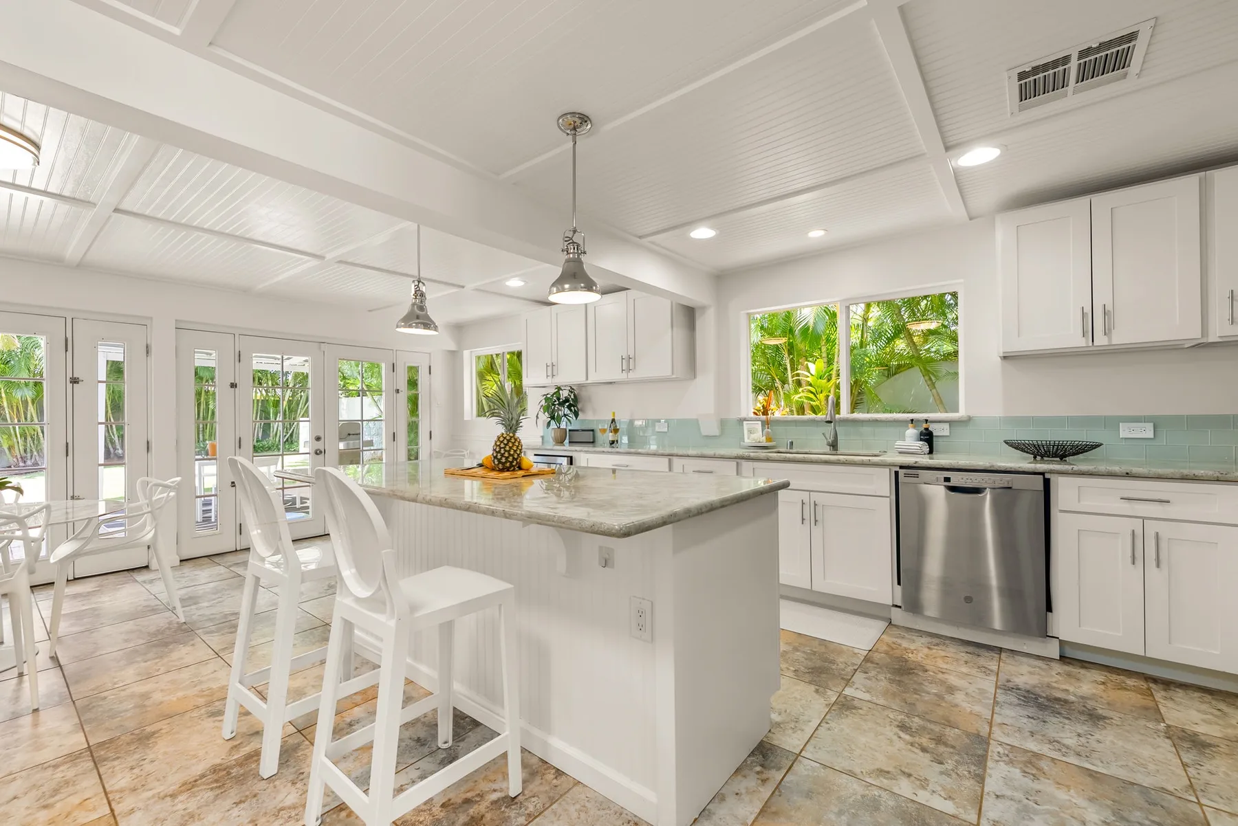 Una cocina luminosa con una isla grande, gabinetes blancos y ventanas con vista a la vegetación.