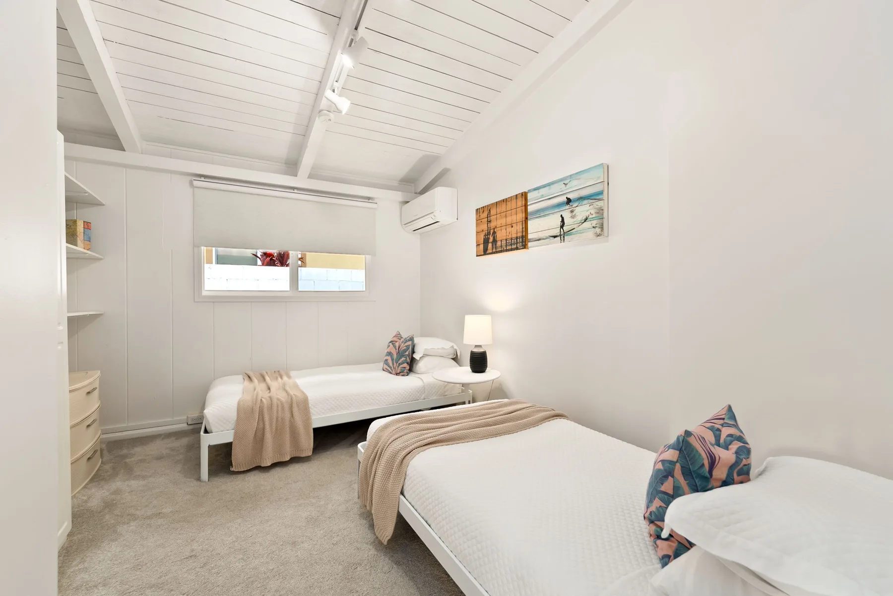 Un dormitorio luminoso con dos camas individuales y una ventana pequeña.