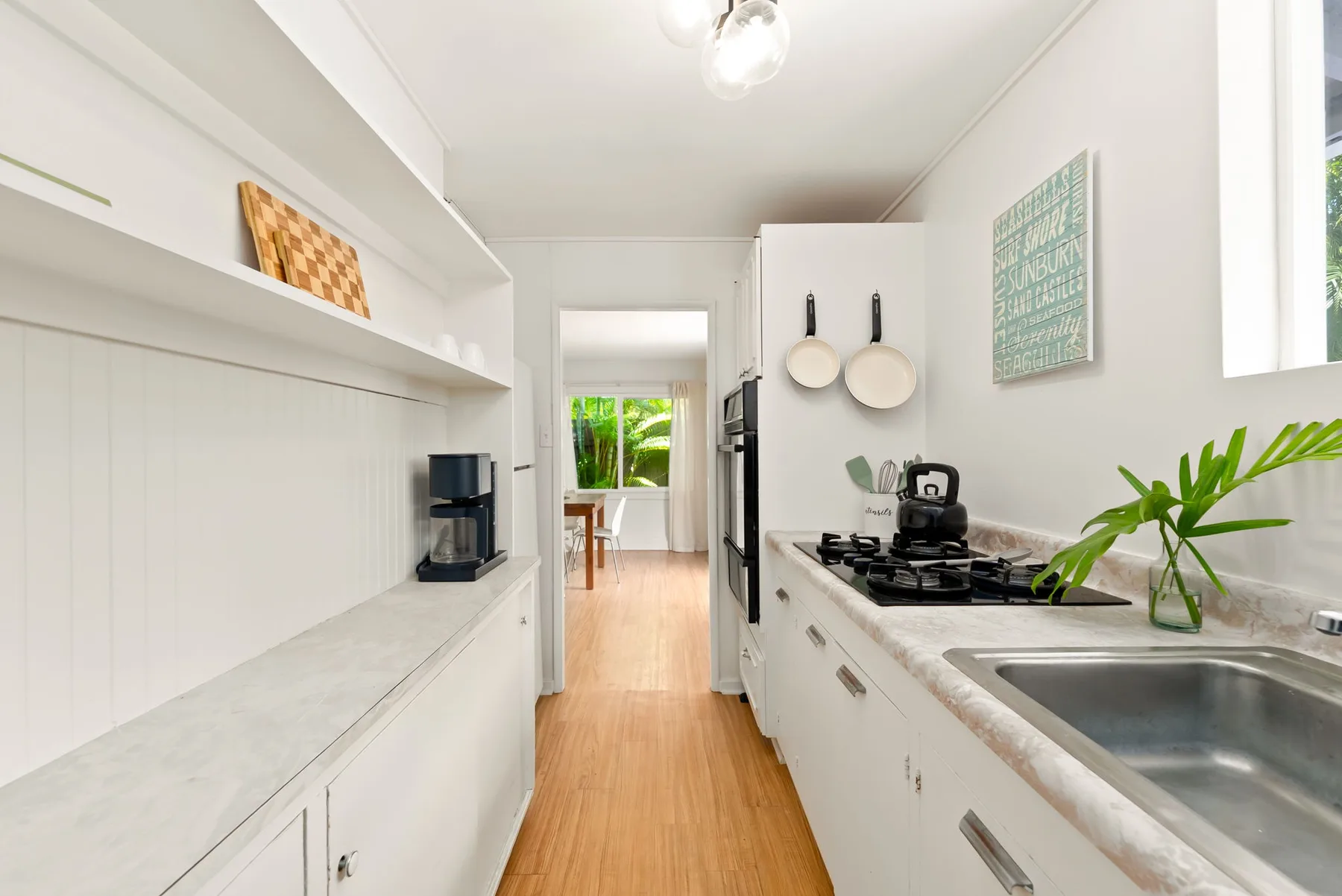 Una cocina alargada y luminosa con gabinetes blancos, una estufa y un fregadero.