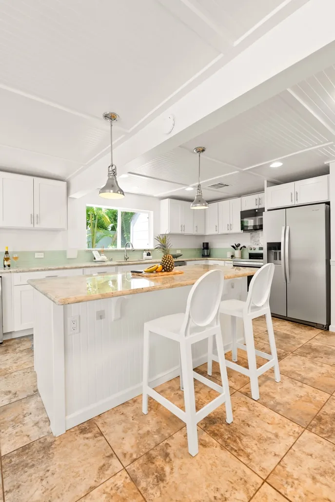 Una cocina luminosa con una isla grande, asientos blancos y electrodomésticos de acero inoxidable.