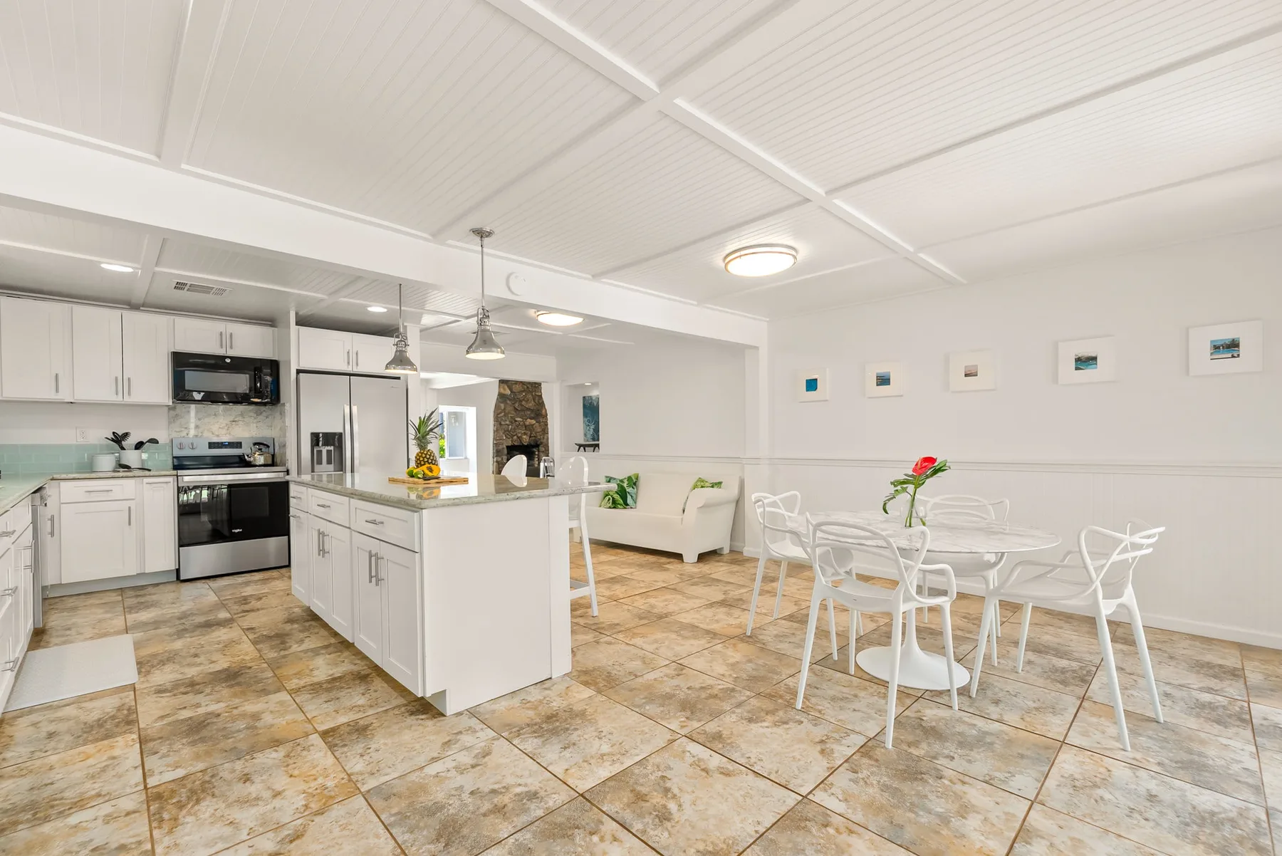 Una cocina abierta y zona de comedor con armarios blancos y suelo de baldosas.
