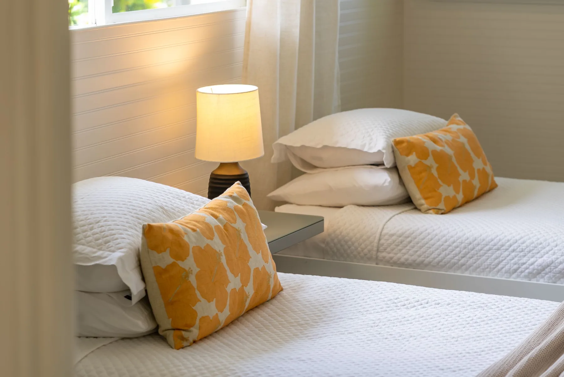 Un dormitorio luminoso con dos camas y cojines decorativos naranjas.