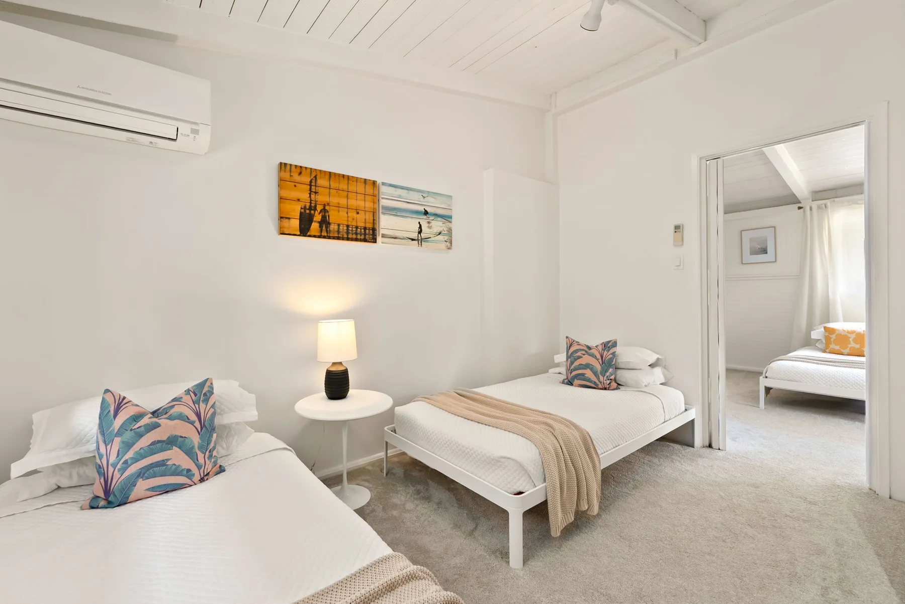 Un dormitorio luminoso con dos camas, cojines estampados y una lámpara de noche.