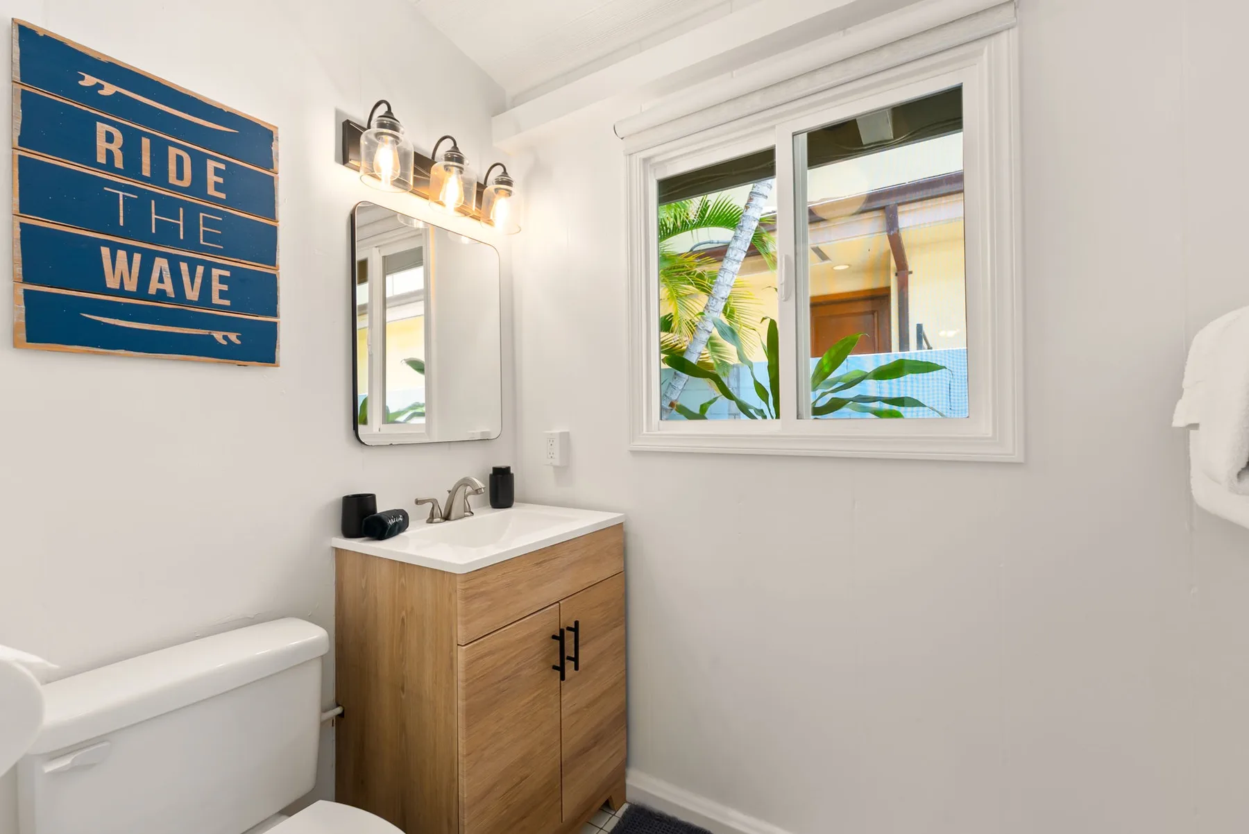 Un baño luminoso con un tocador de madera, espejo y ventana.