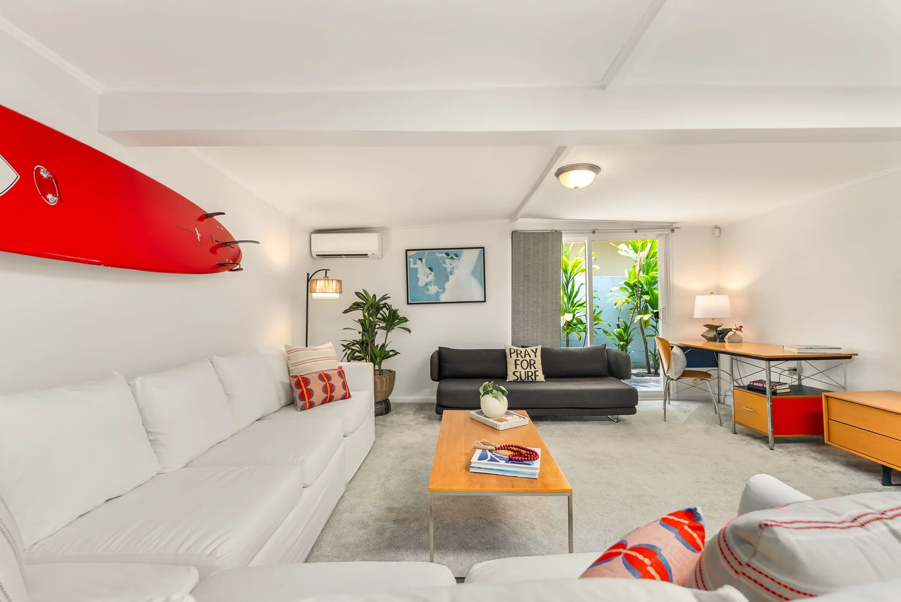 Una sala de estar luminosa con asientos blancos, un sofá oscuro y una mesa de centro.