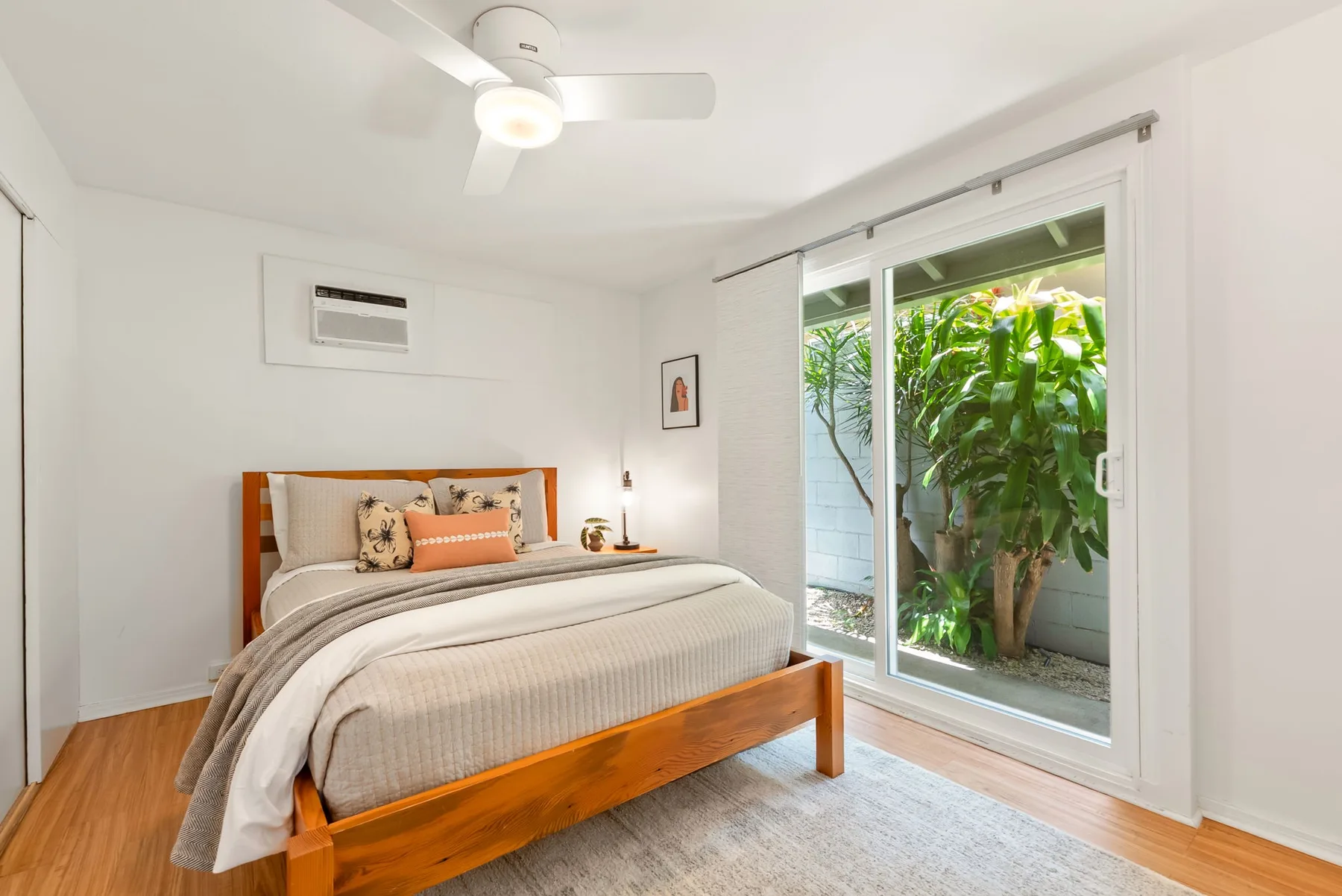 Un dormitorio con una cama de madera junto a una gran puerta de vidrio con vista a la vegetación.